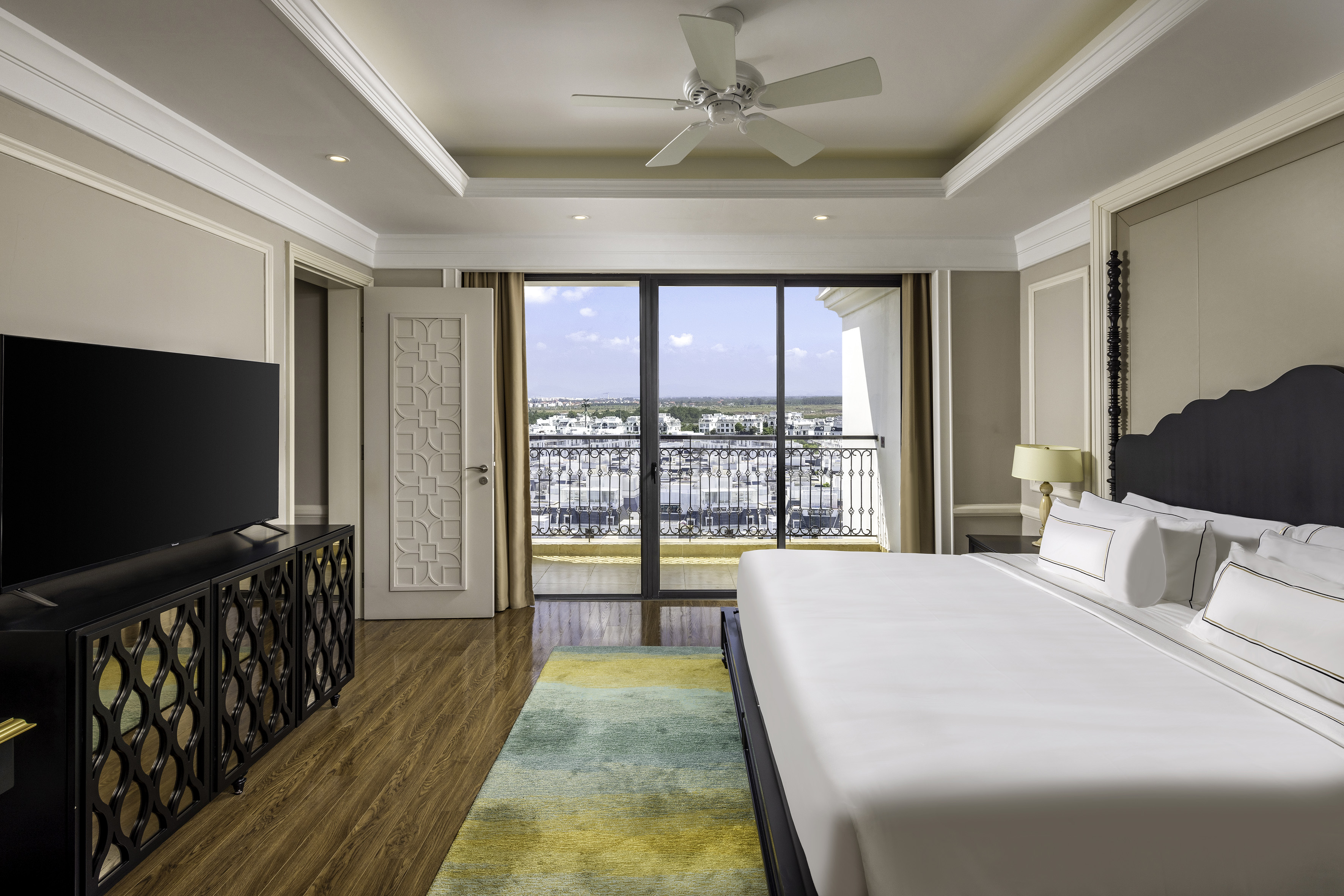 Hotel bedroom with king bed, balcony view, TV, and stylish decor.