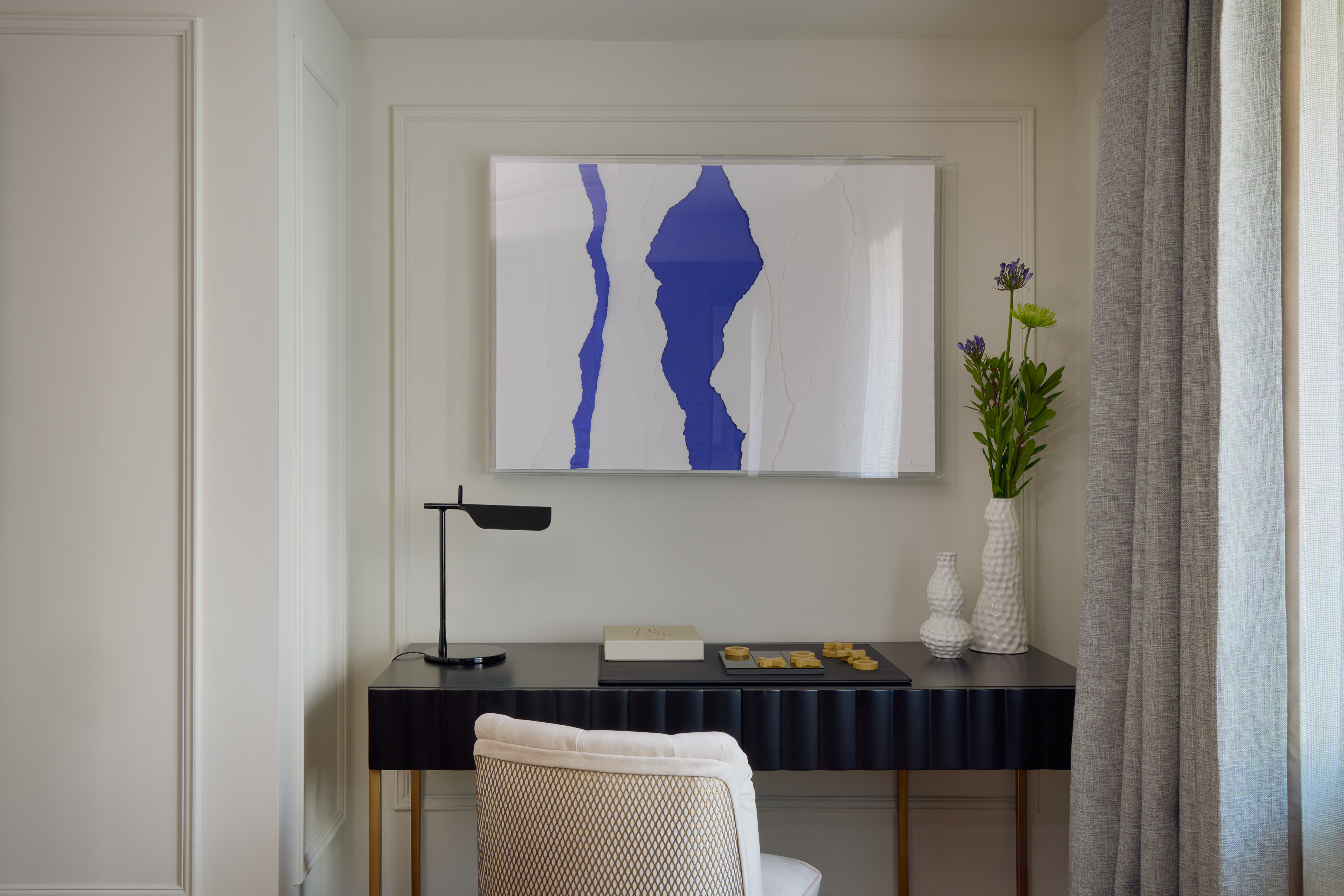 Black console desk with blue abstract art, modern lamp, and flowers.