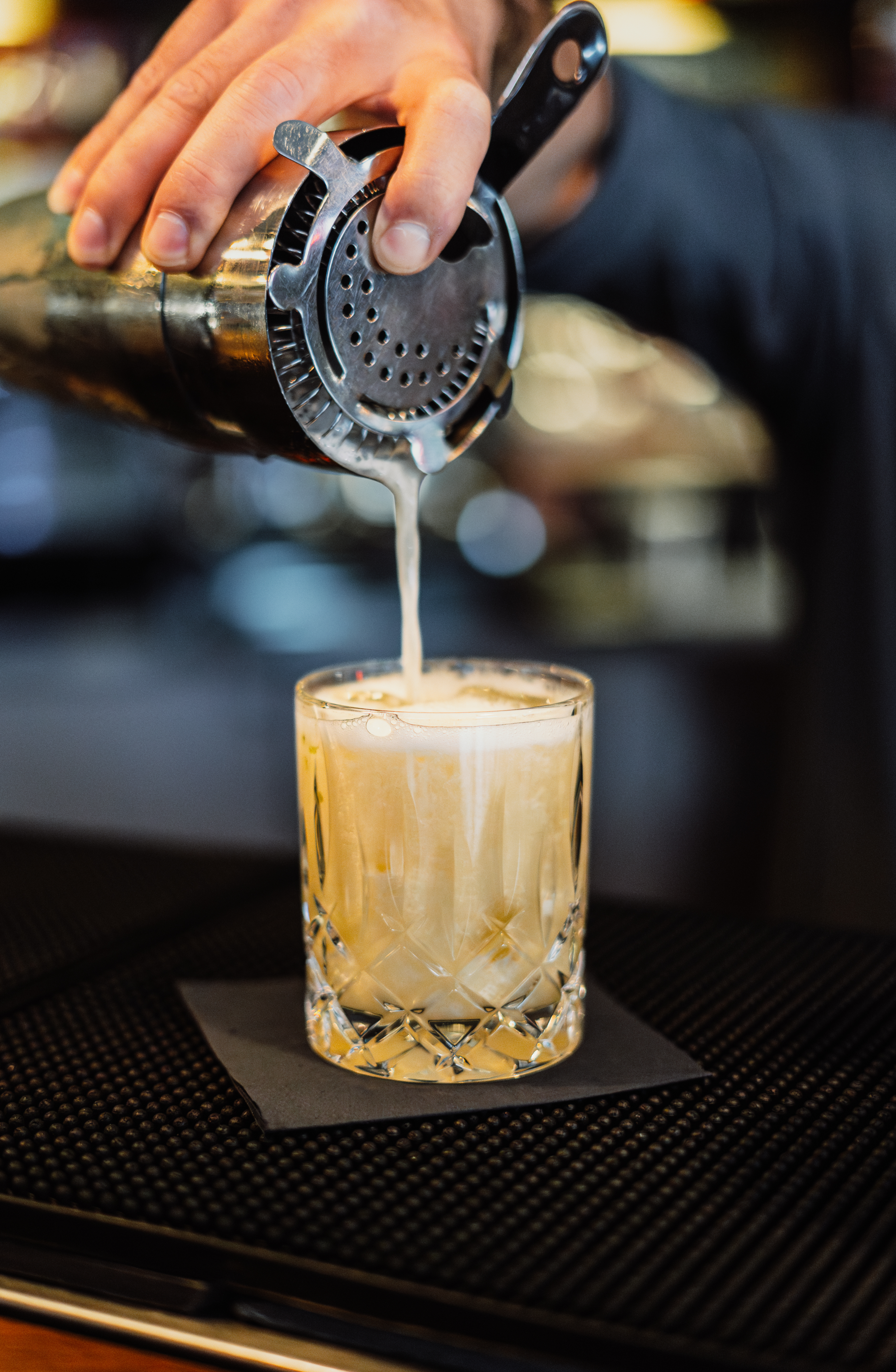 Bartender pouring craft cocktail from shaker into a faceted glass at a bar. - Happy 2027! - Meliá Berlin, Berlin