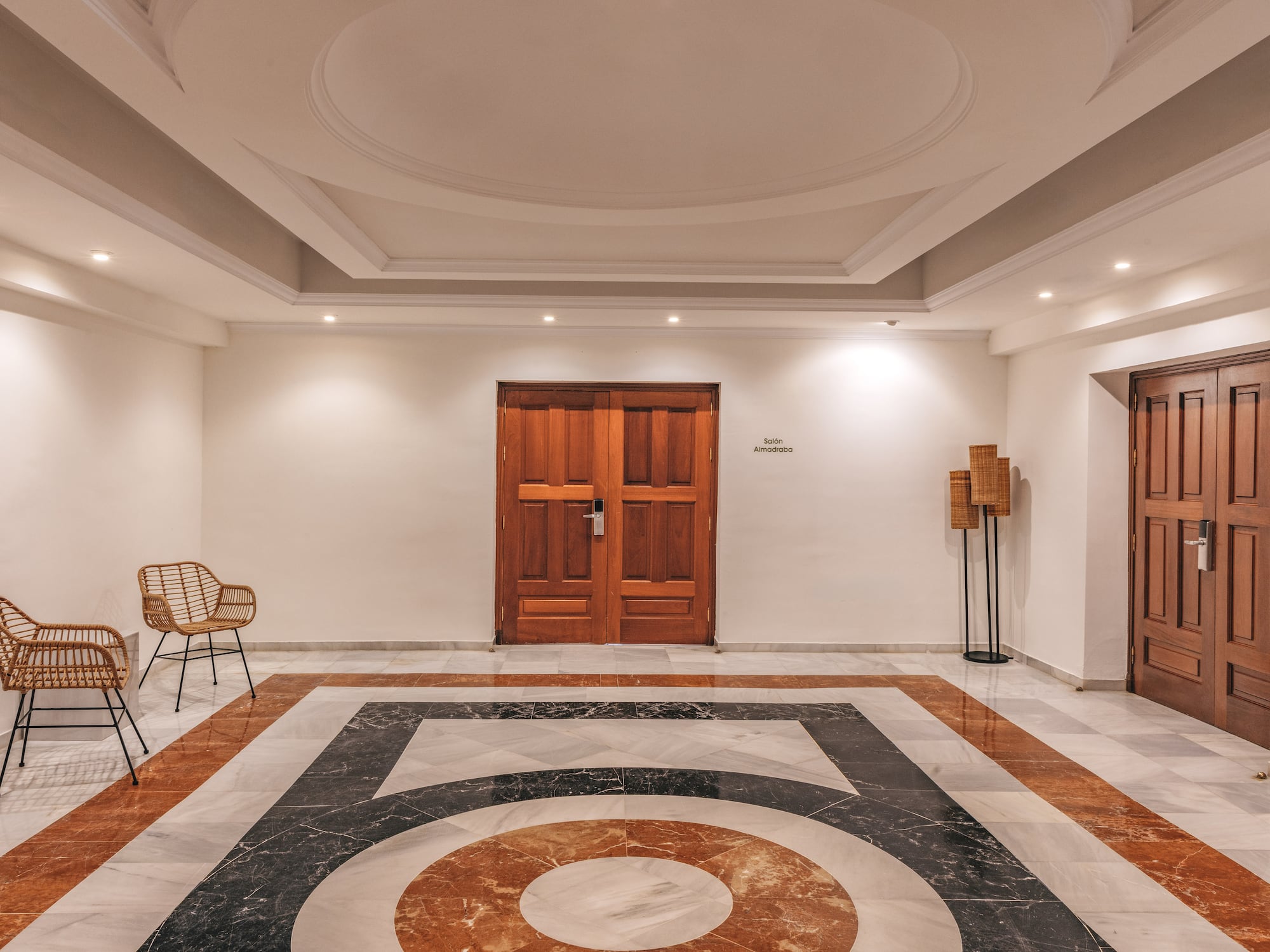 Conference lobby with geometric marble floor, wooden doors, and wicker chairs.