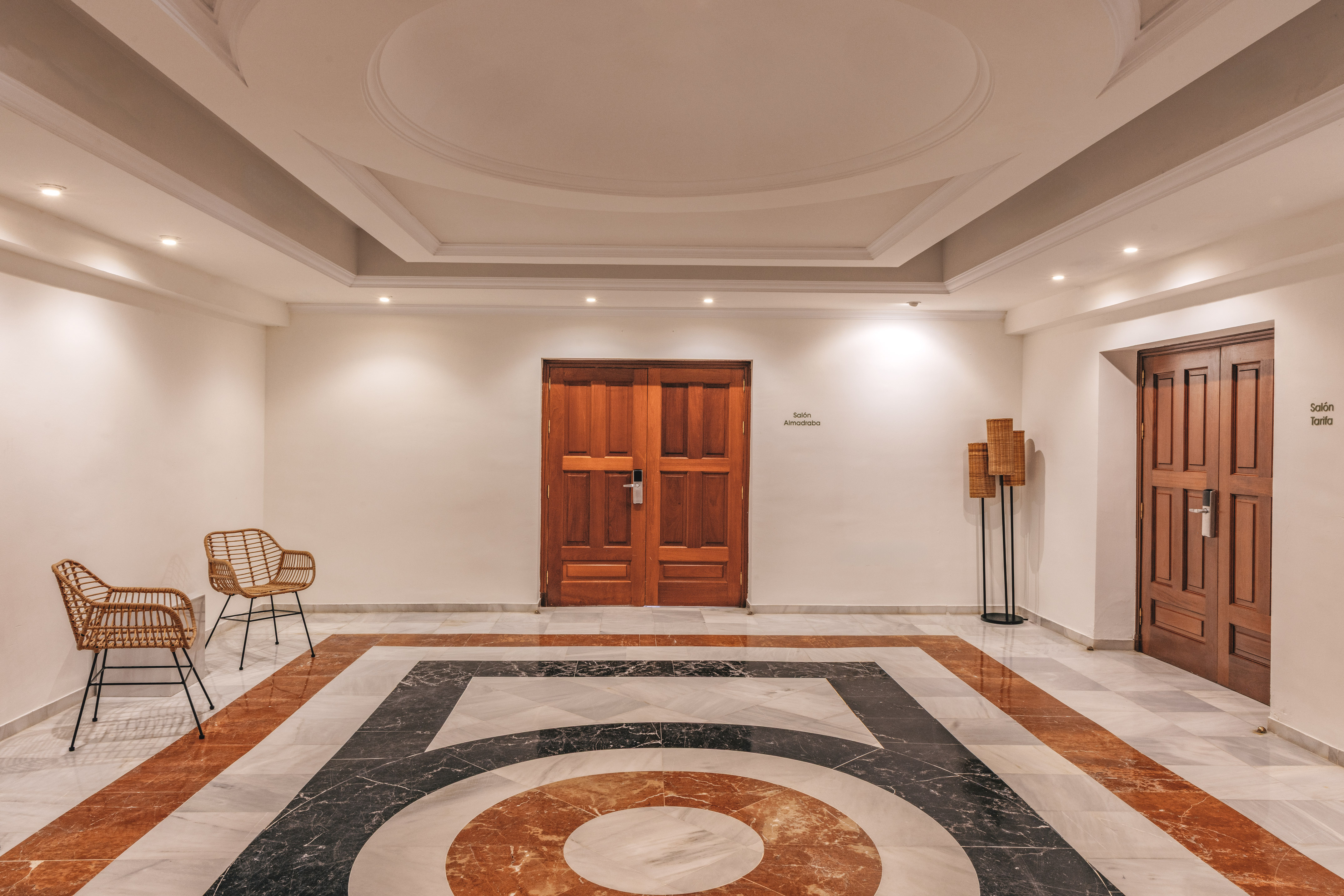 Conference lobby with geometric marble floor, wooden doors, and wicker chairs.