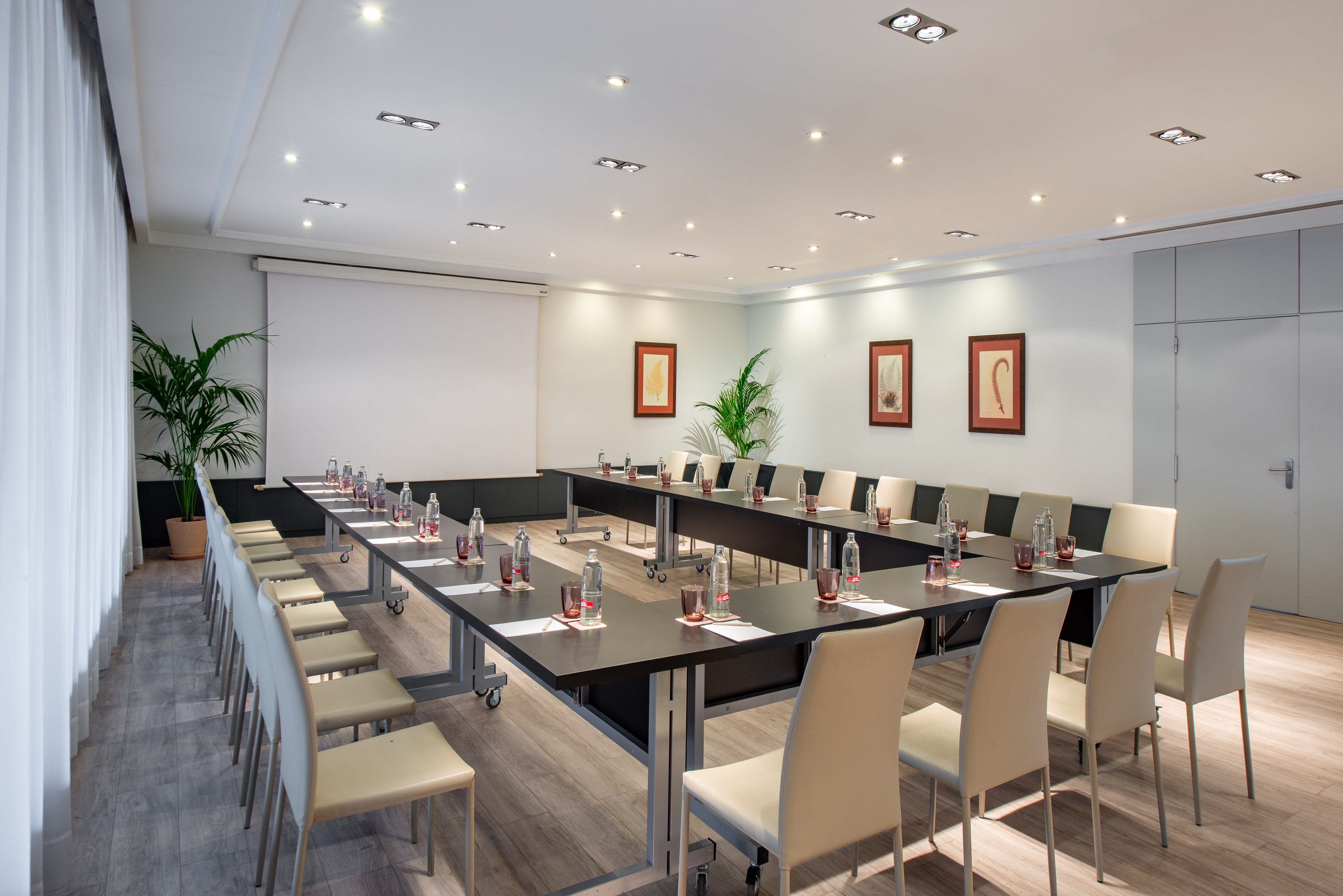 Modern U-shape conference room setup with tables, chairs, and projector screen.