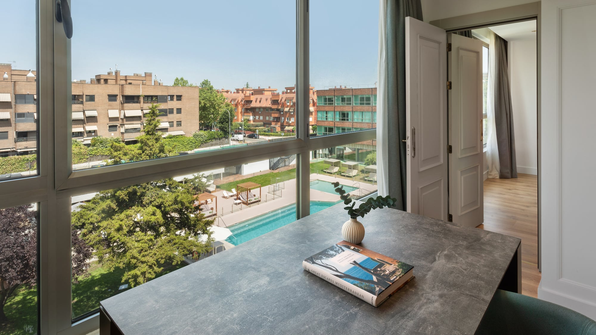 a table with a book on it and a window with a view of a pool and trees