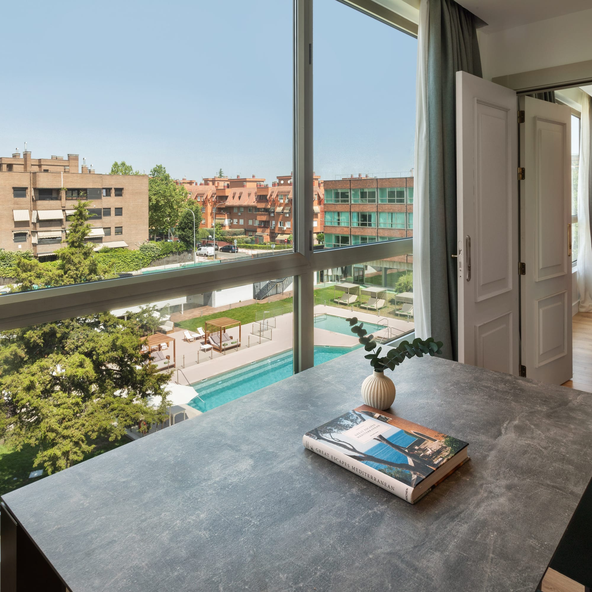 a table with a book on it and a window with a view of a pool and trees