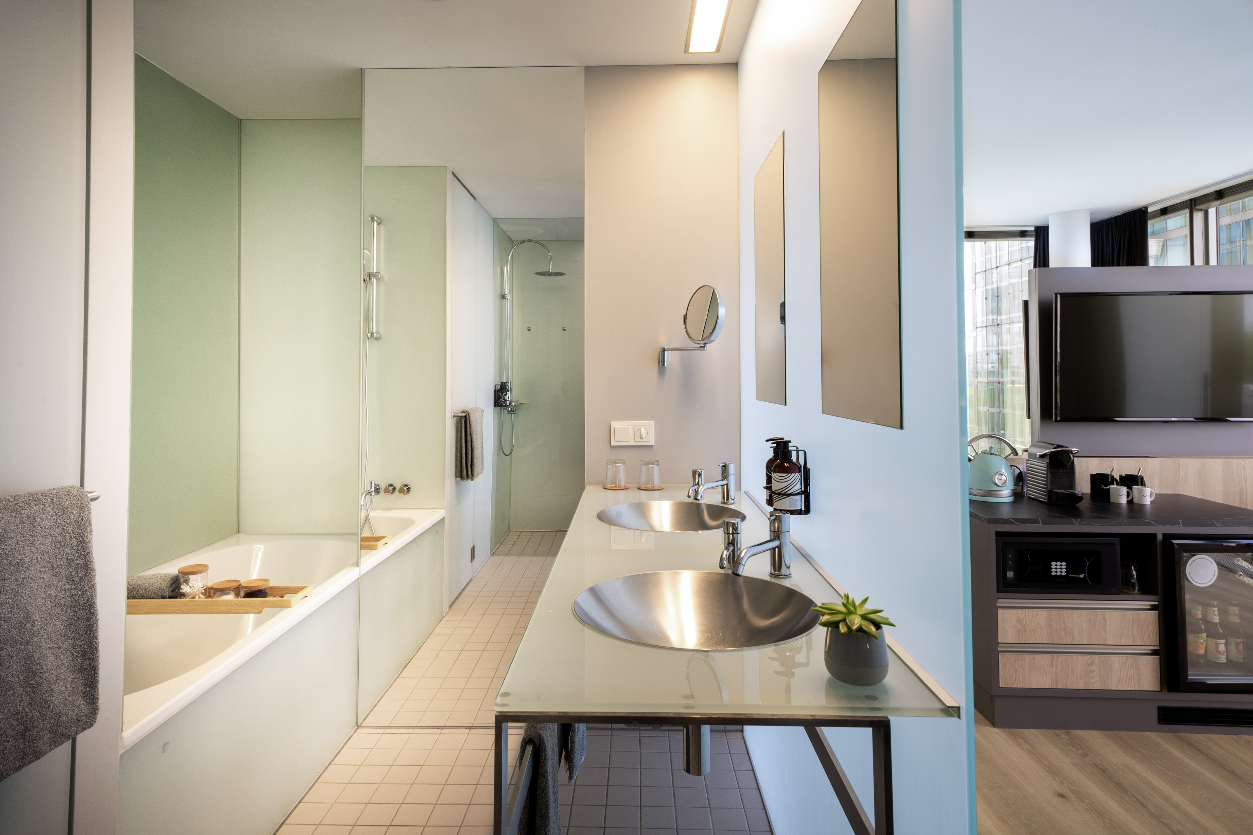 Modern hotel bathroom with double vanity, bathtub, shower, and kitchenette area.