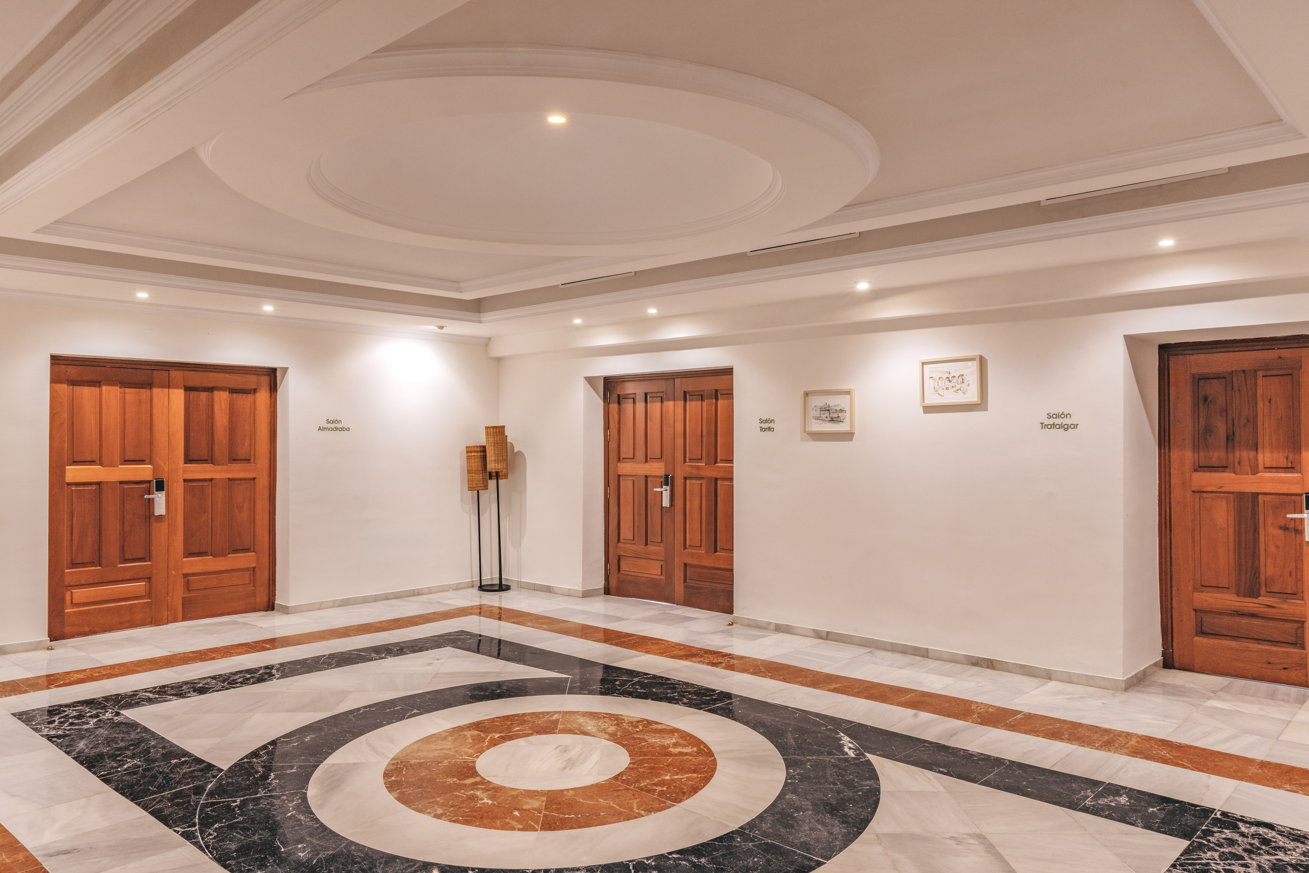 Elegant hotel corridor with patterned marble floor and wooden doors to meeting rooms.