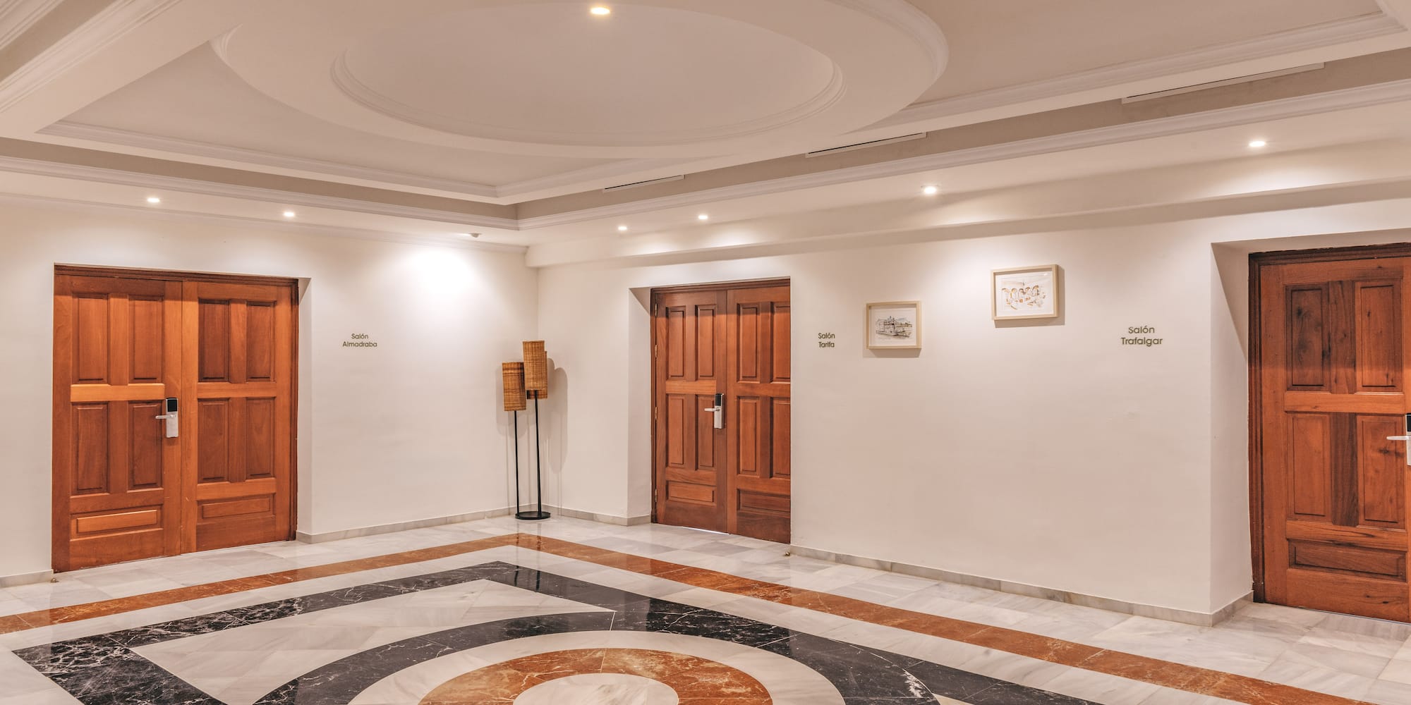 Elegant hotel corridor with patterned marble floor and wooden doors to meeting rooms.
