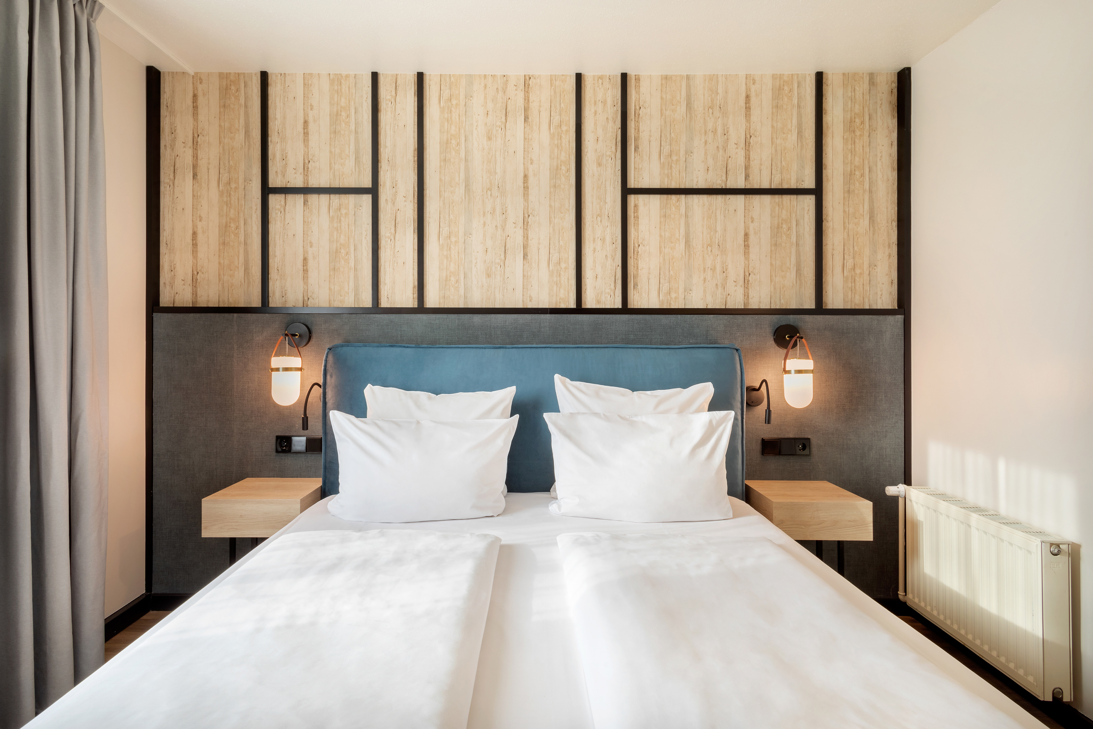 Modern hotel room with blue headboard, wood accent wall, and white bed.