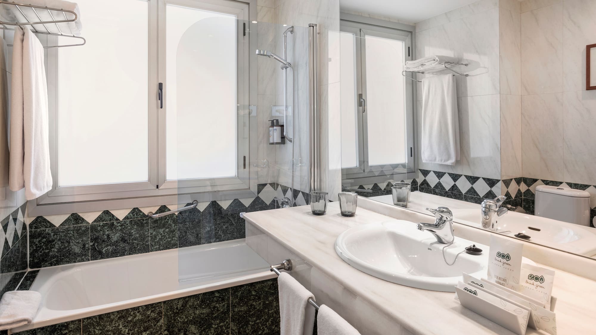Hotel bathroom with bathtub, shower, marble vanity, sink, and green tiled walls.
