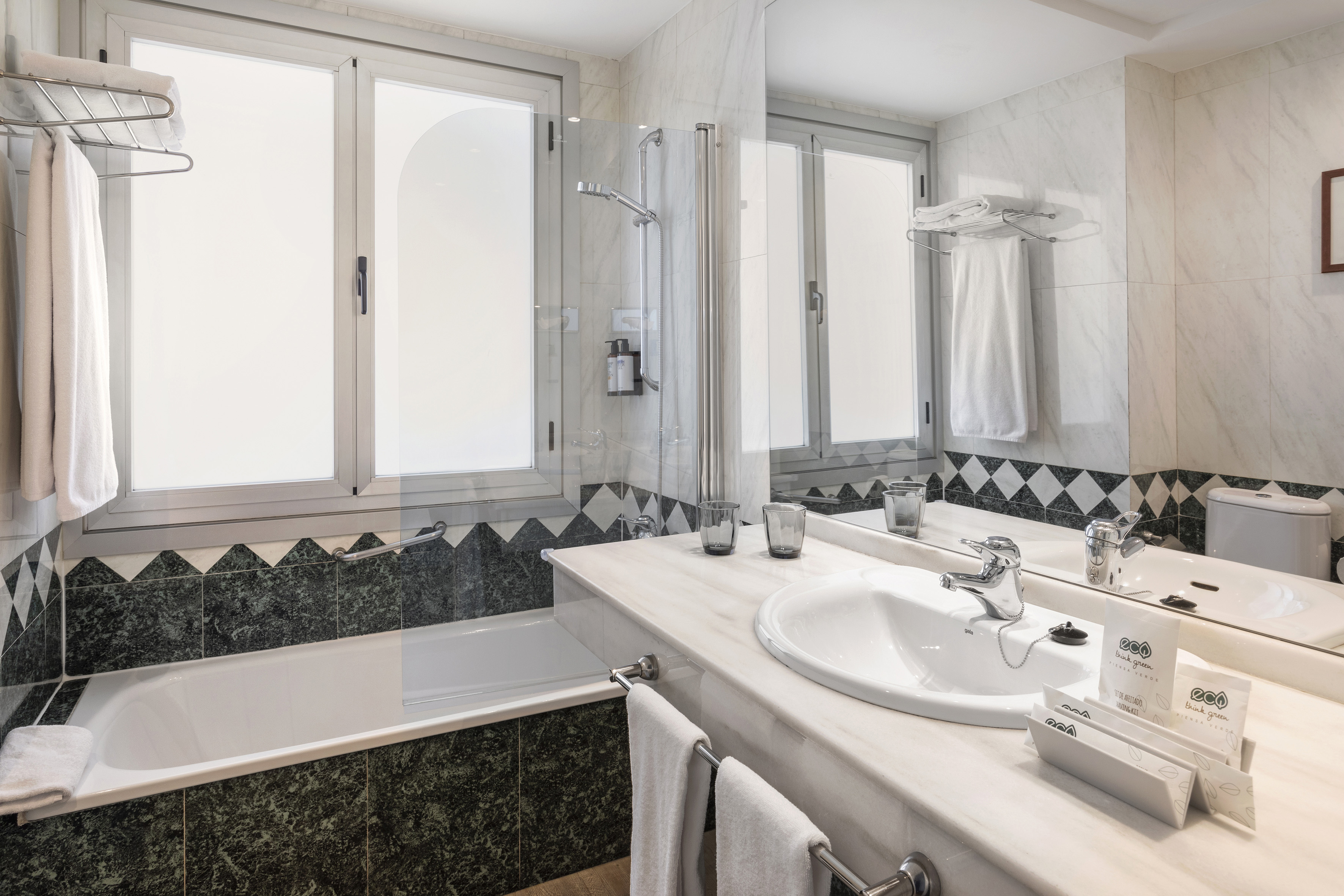 Hotel bathroom with bathtub, shower, marble vanity, sink, and green tiled walls.