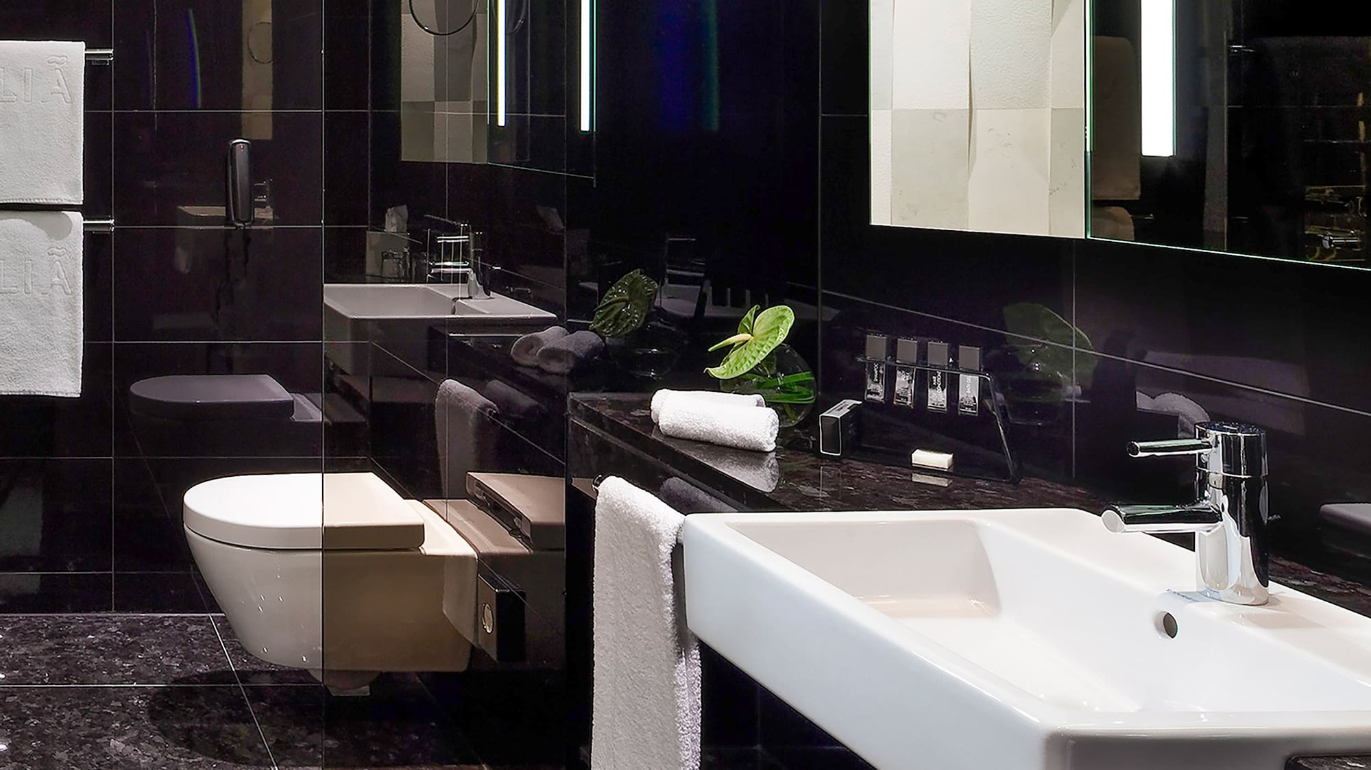 Sleek black bathroom with white sink, toilet, and lighted vanity mirror.