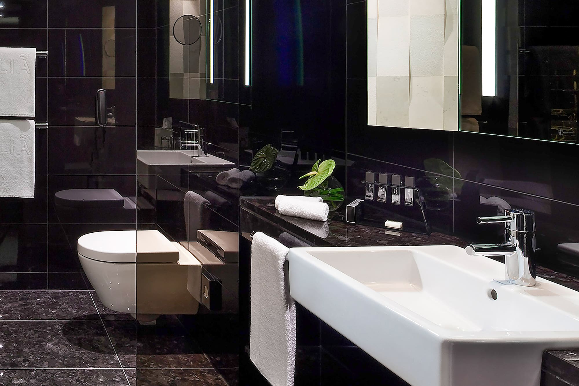 Sleek black bathroom with white sink, toilet, and lighted vanity mirror.