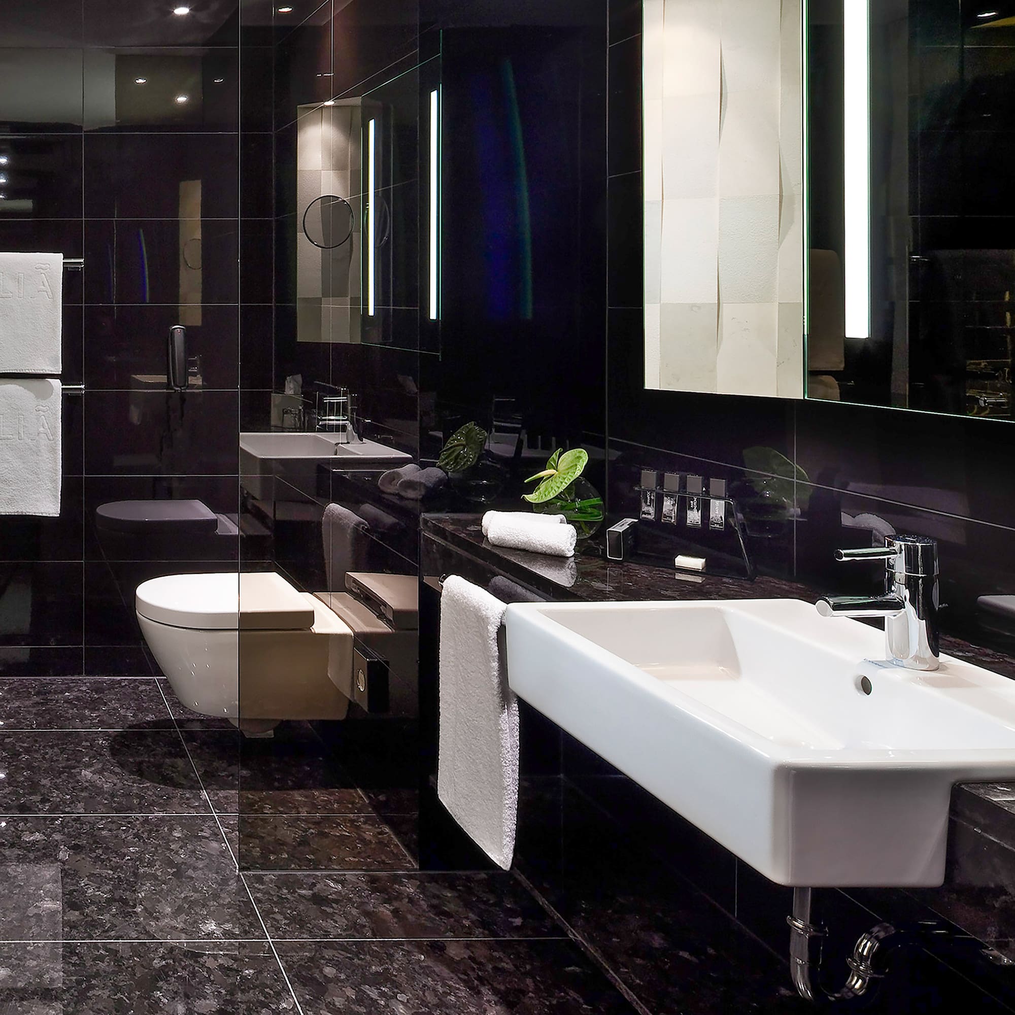 Sleek black bathroom with white sink, toilet, and lighted vanity mirror.