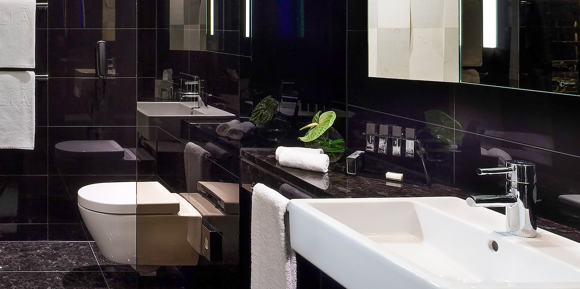 Sleek black bathroom with white sink, toilet, and lighted vanity mirror.
