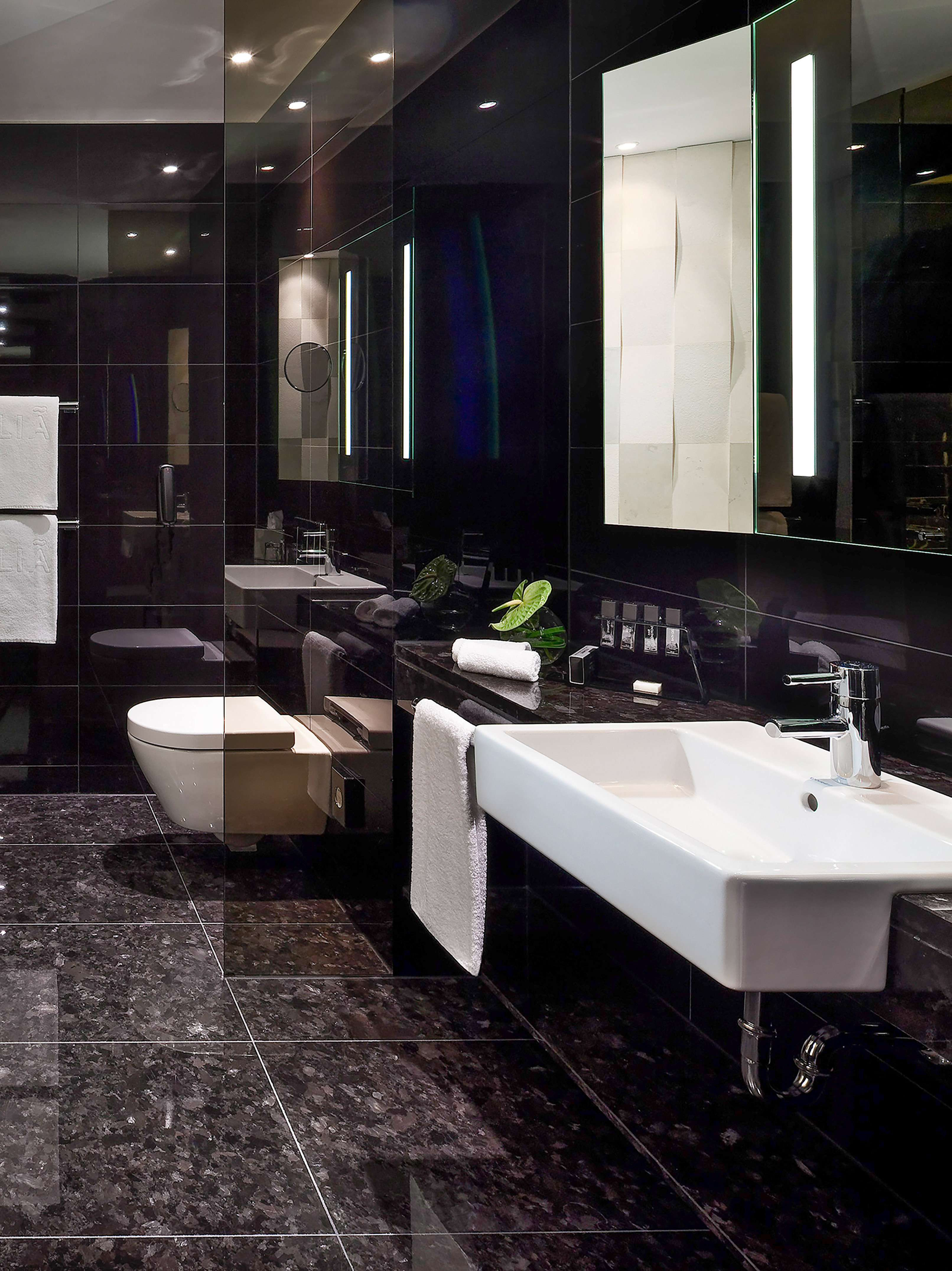 Sleek black bathroom with white sink, toilet, and lighted vanity mirror.