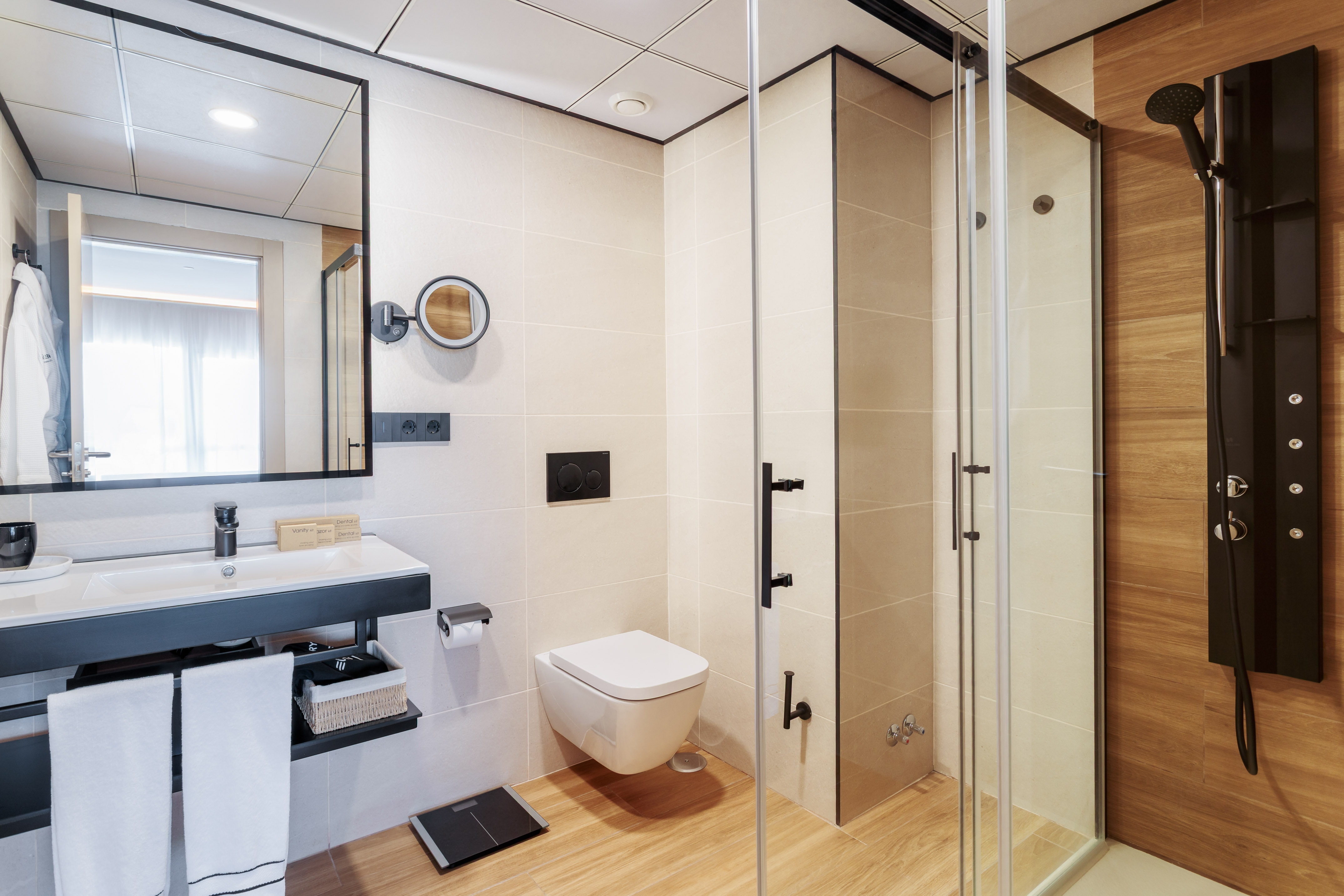 Modern hotel bathroom with vanity, wall-mounted toilet, and glass shower.