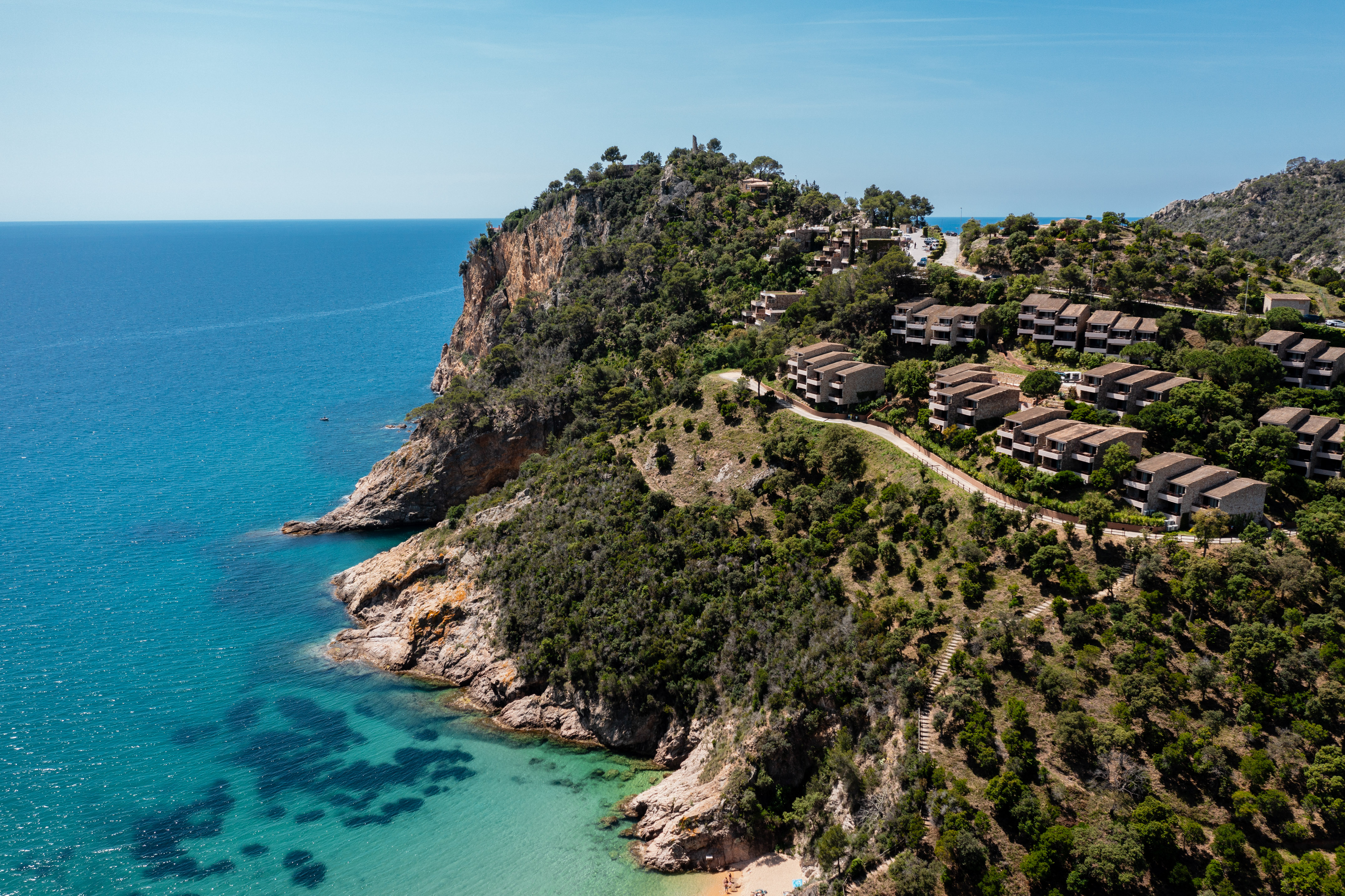 Mediterranean coastal resort with hillside villas, turquoise sea, and sandy beach.