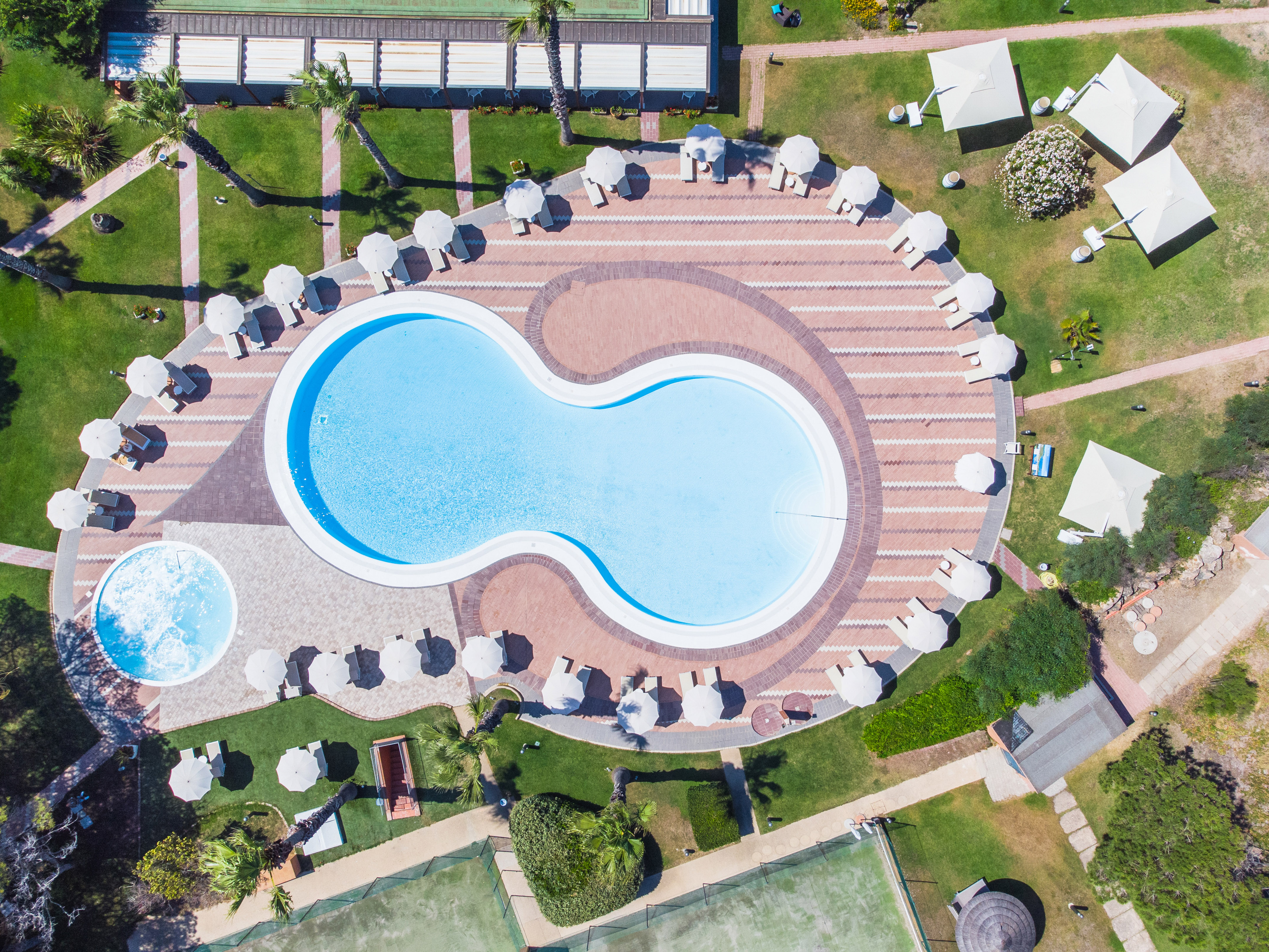 Aerial resort view: large swimming pool, lounge chairs, umbrellas, tennis courts.