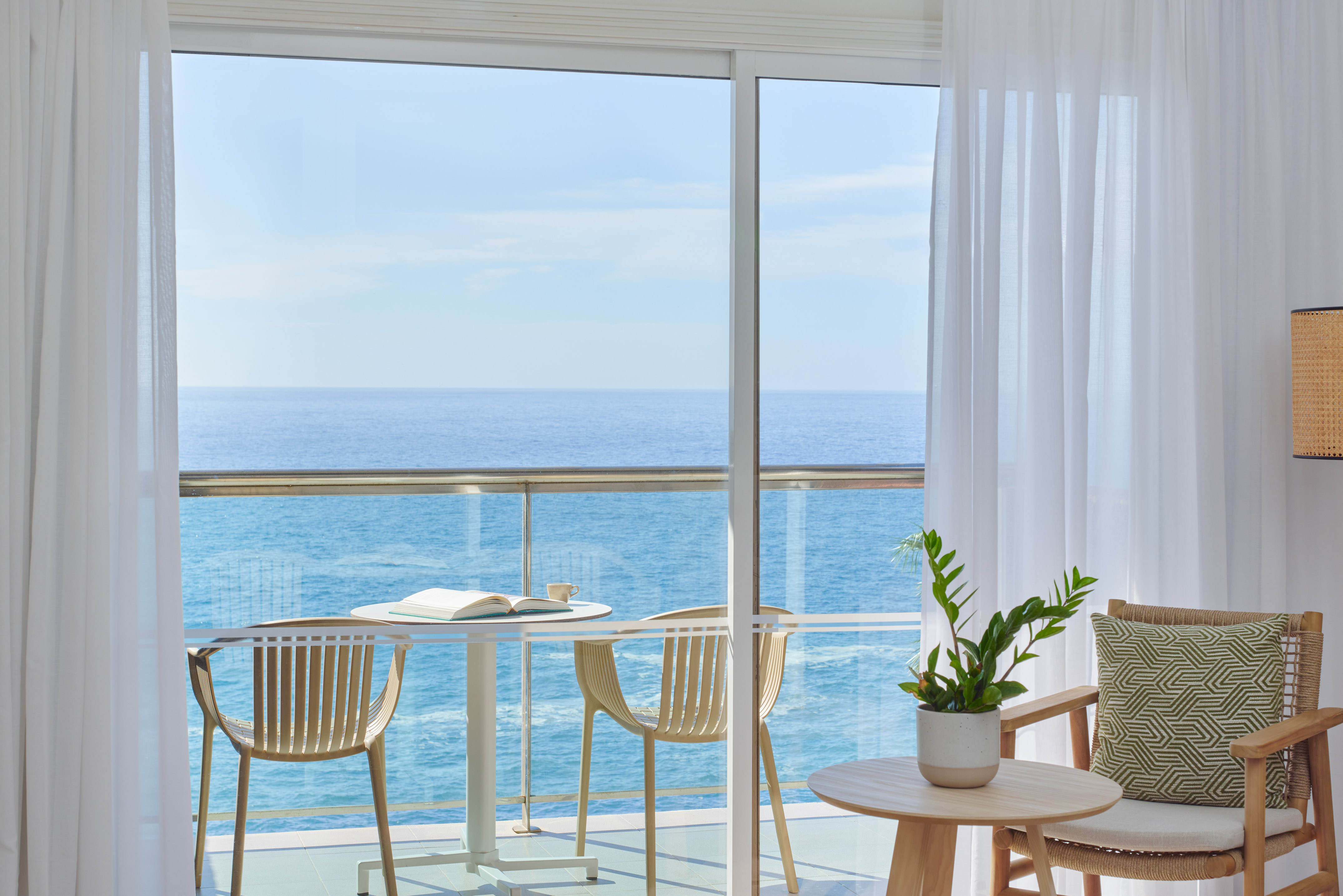 Ocean view balcony with table, chairs, book, and sheer white curtains.