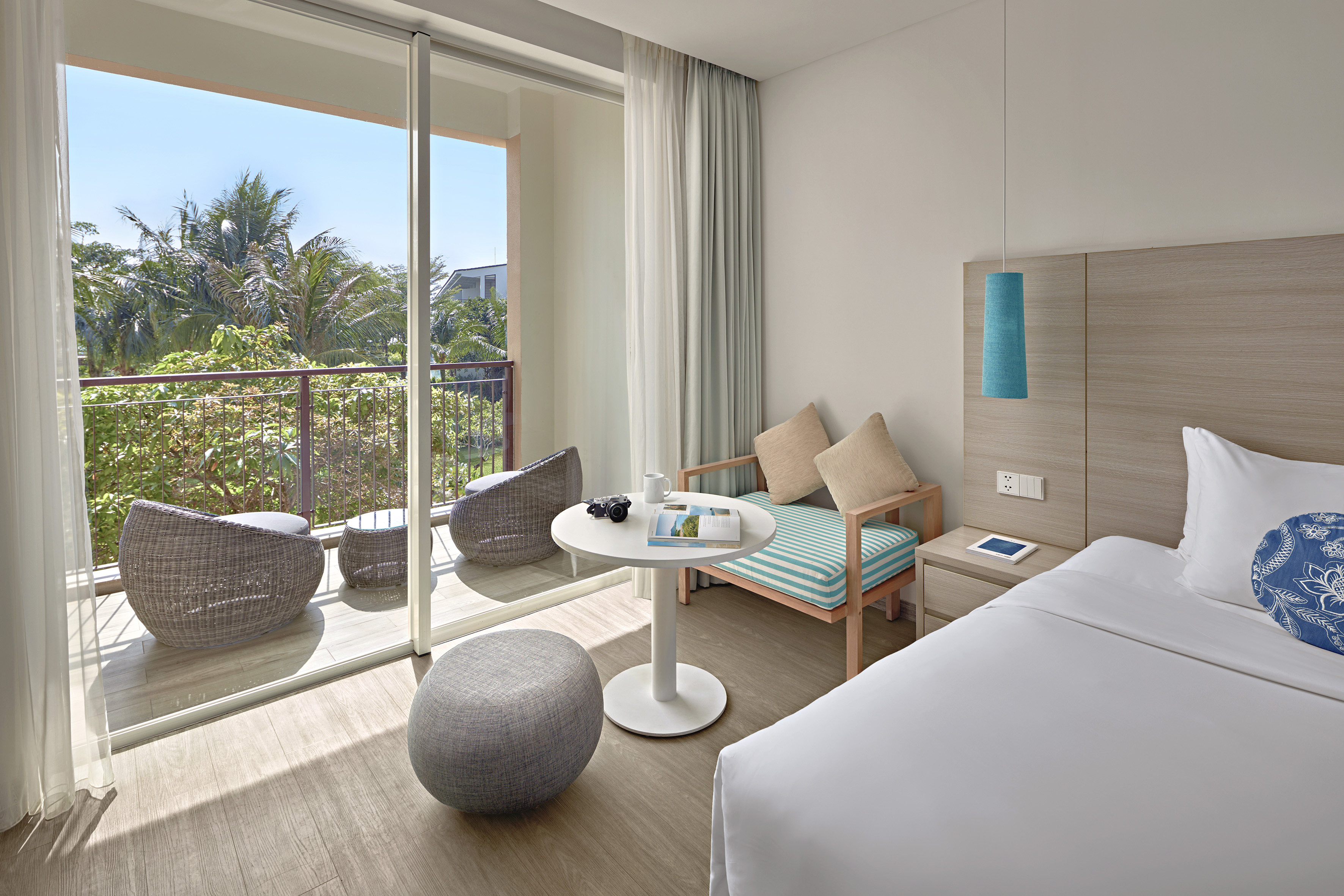 Modern resort room with balcony overlooking tropical greenery.