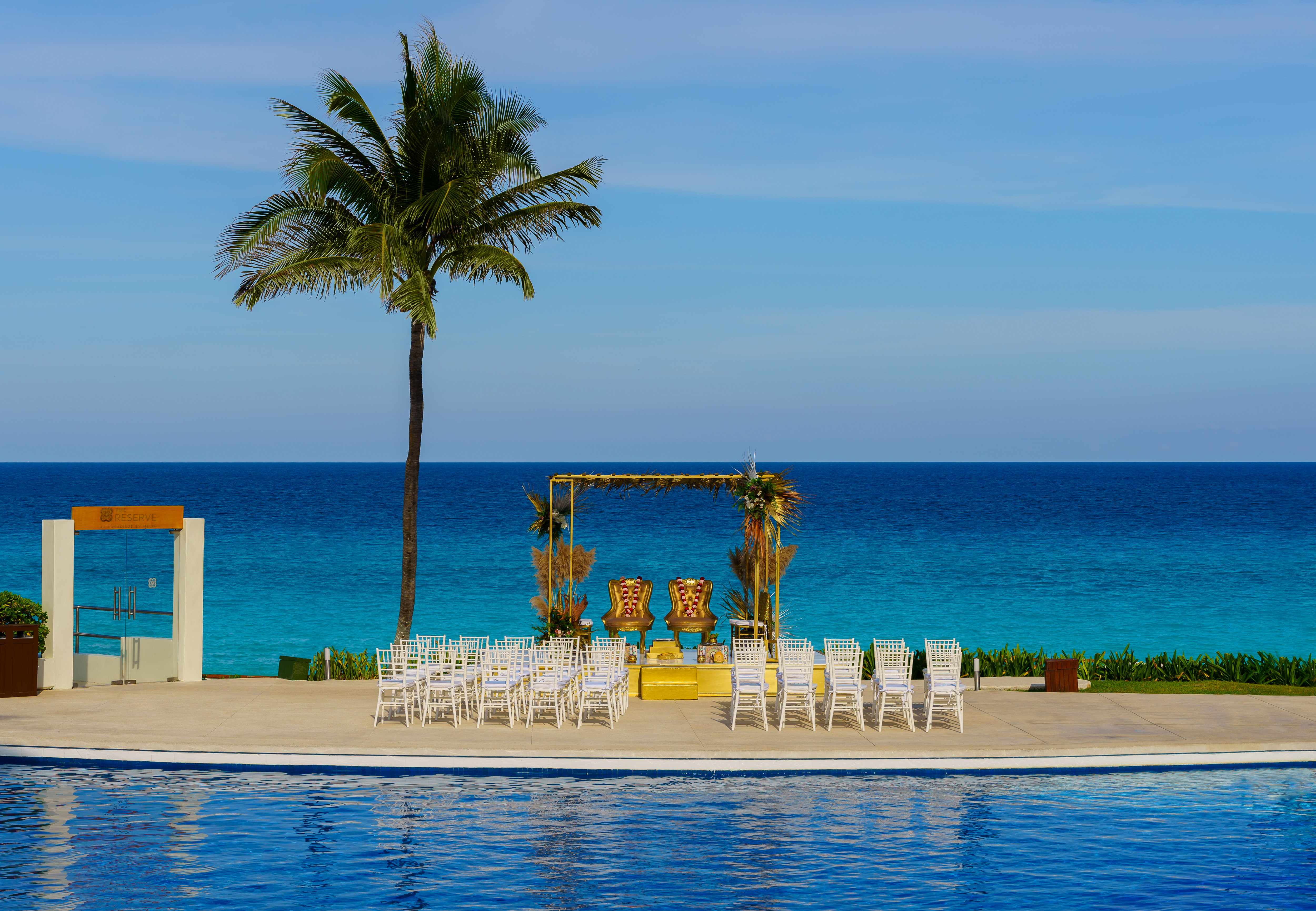 Beach wedding ceremony setup overlooking turquoise ocean and pool.
