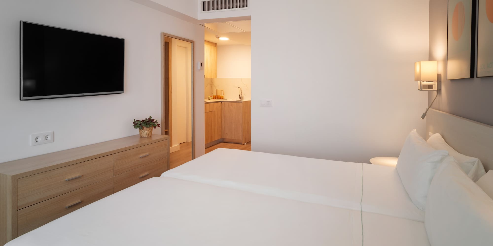 Bright studio apartment with two single beds, TV, and kitchenette.