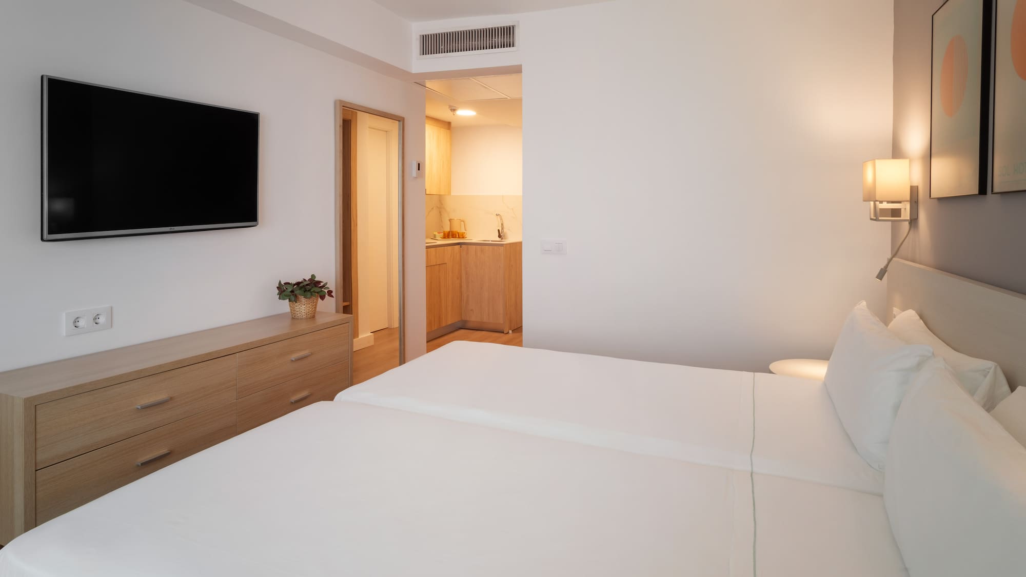 Bright studio apartment with two single beds, TV, and kitchenette.