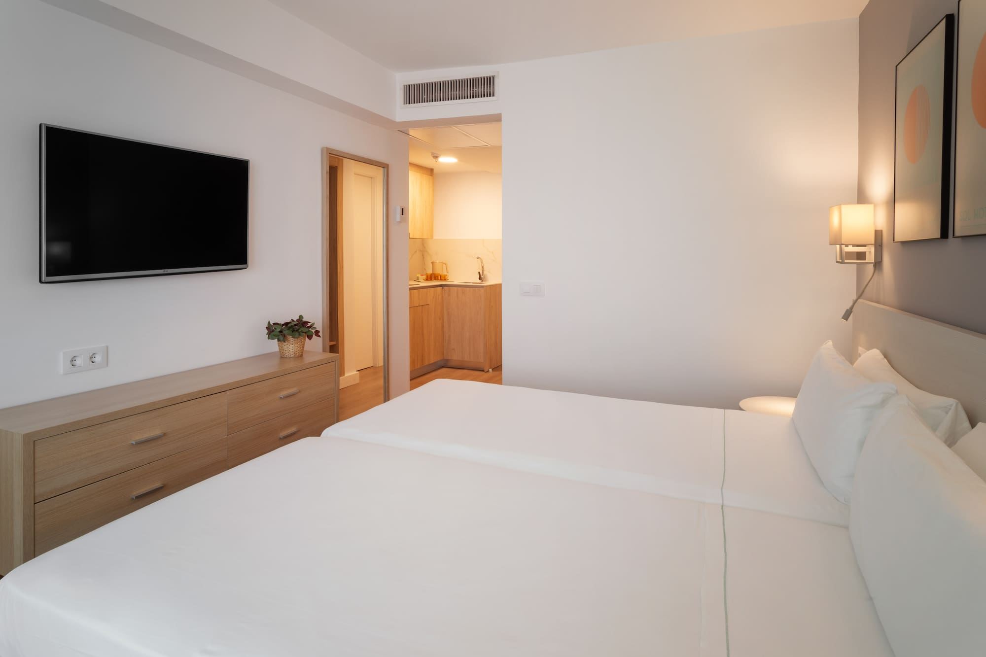 Modern hotel studio with twin beds, TV, dresser, and kitchenette.