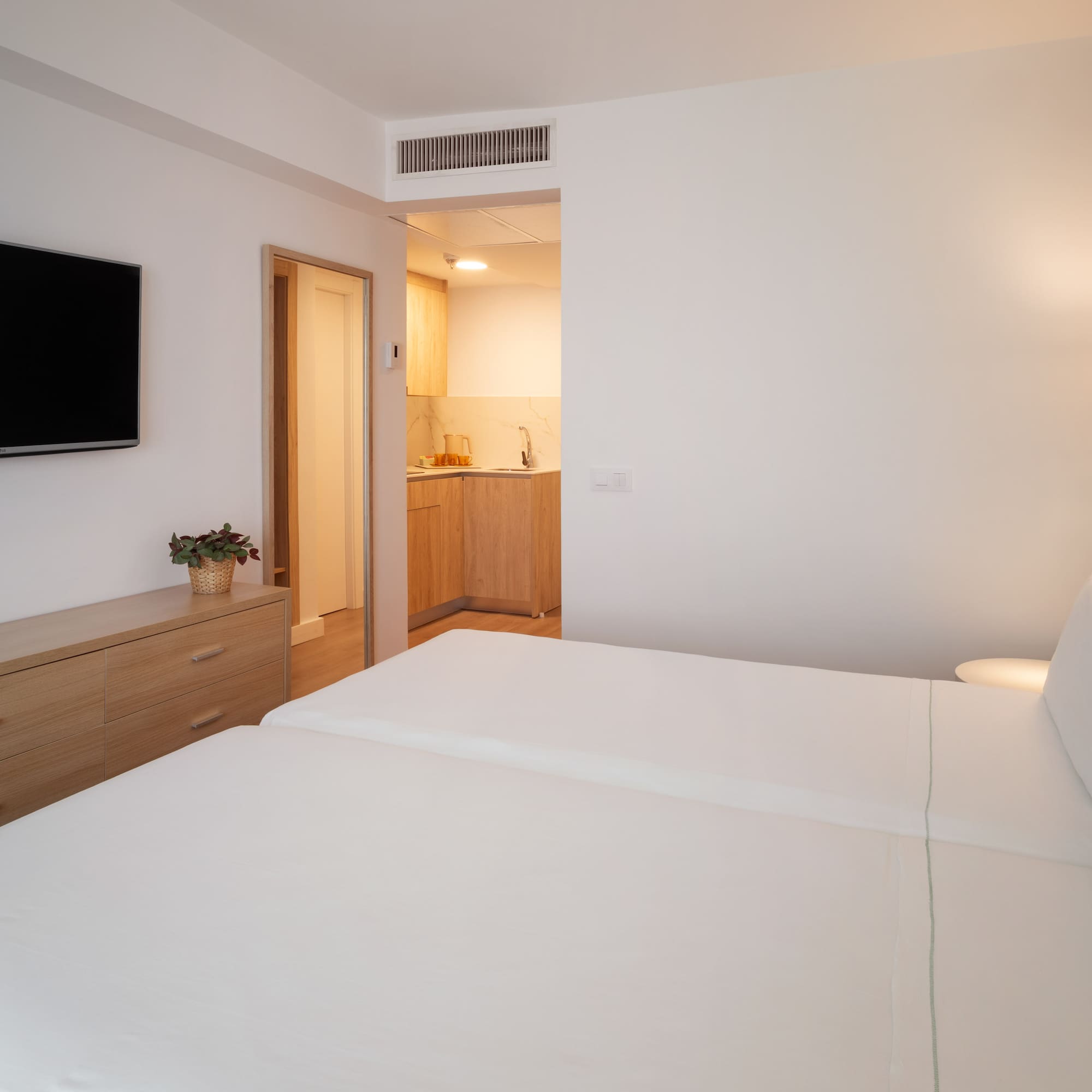 Bright studio apartment with two single beds, TV, and kitchenette.