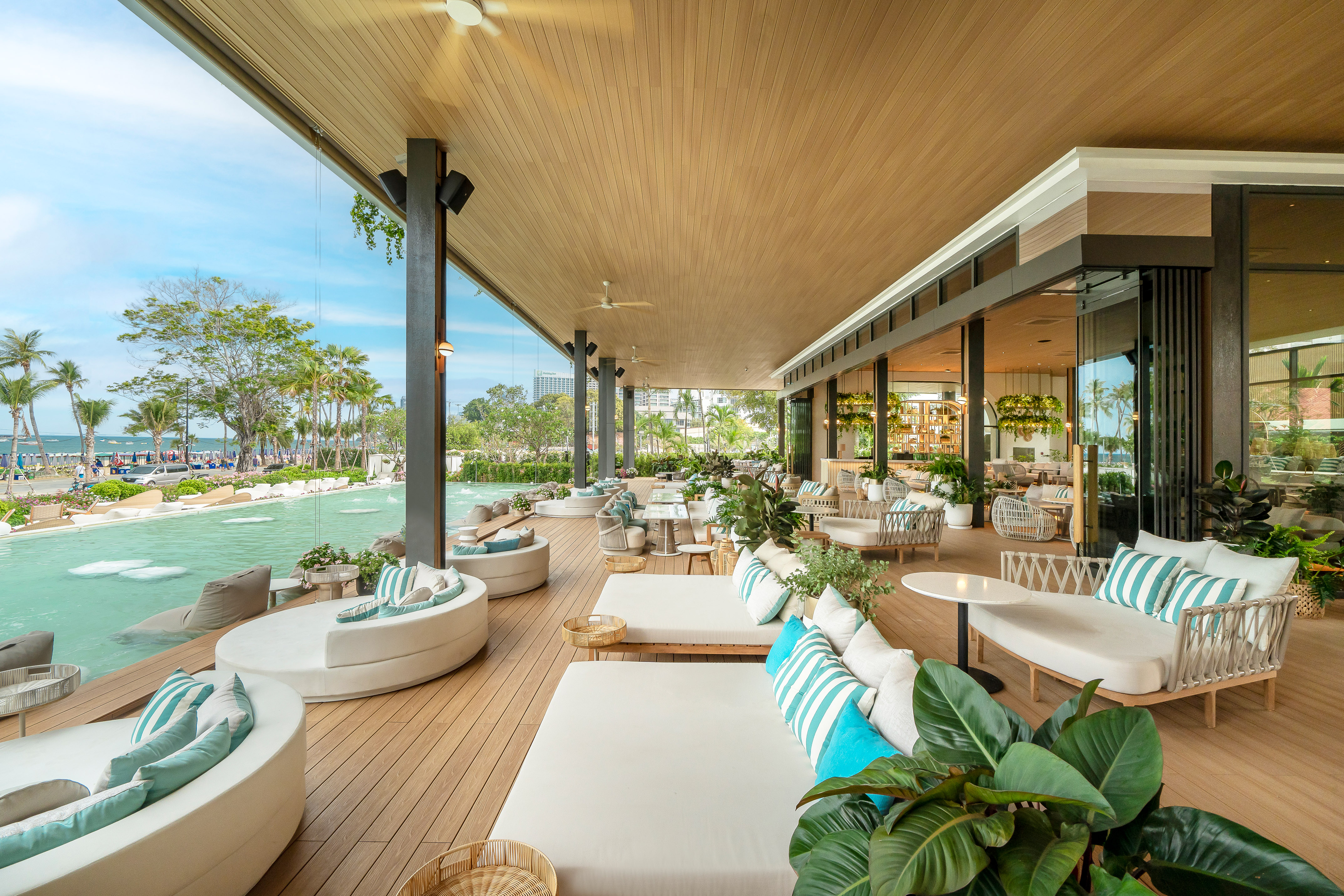 Luxury resort outdoor lounge overlooking beach, pool, with stylish deck seating.