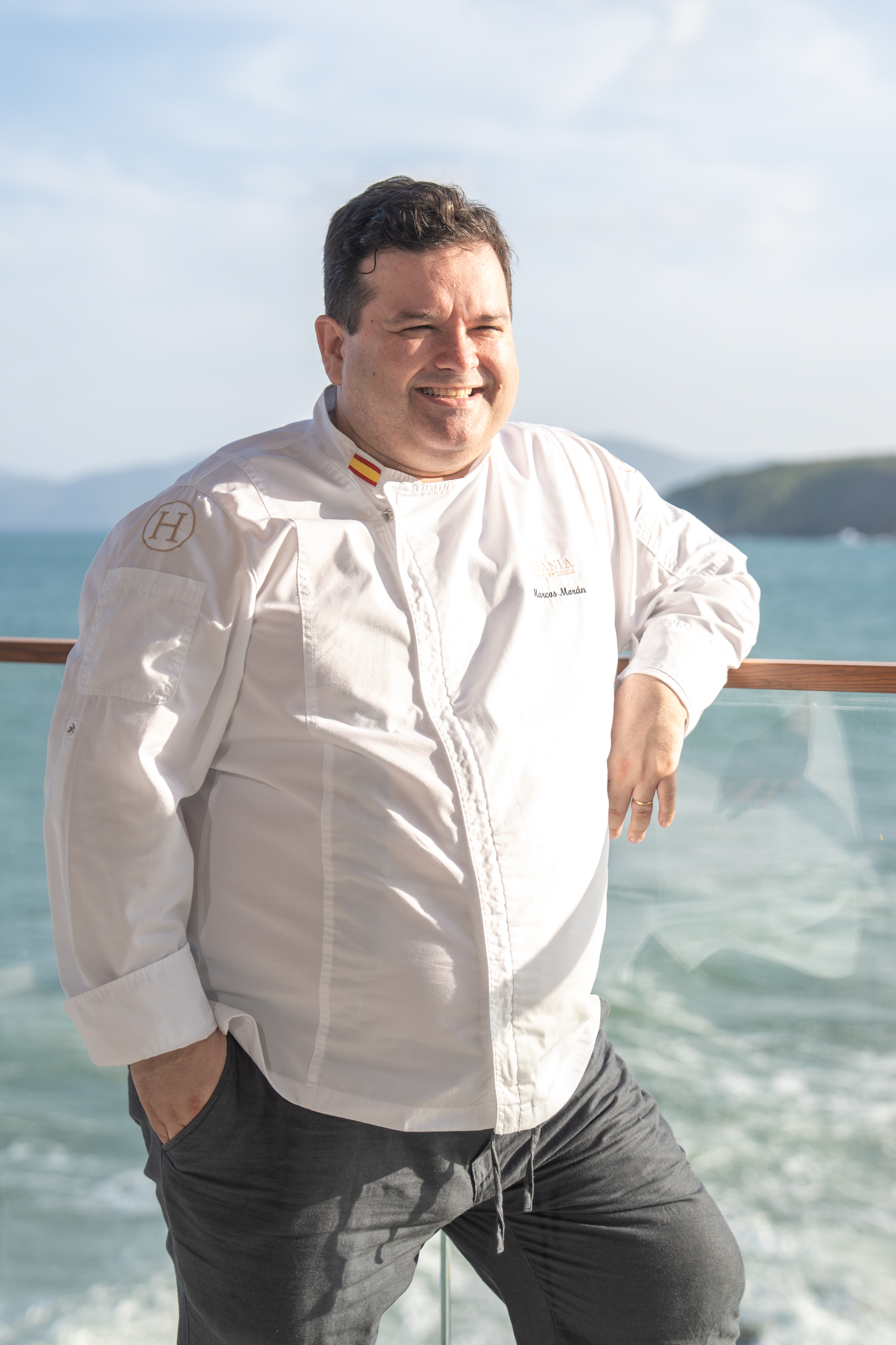 Spanish chef Marcos Morán in white uniform smiling by the sea.