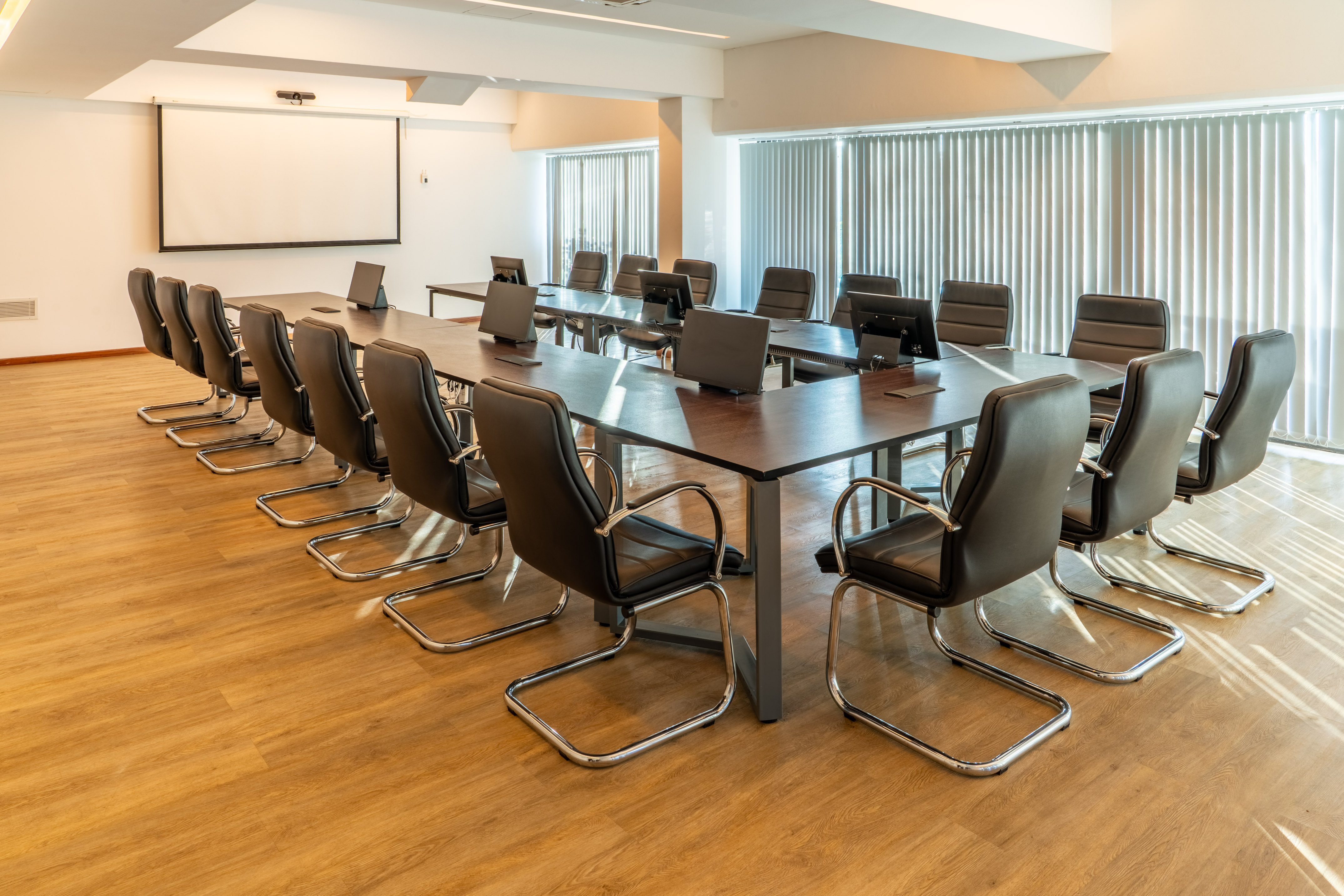 Modern conference room, U-shaped table, black executive chairs, projector screen.