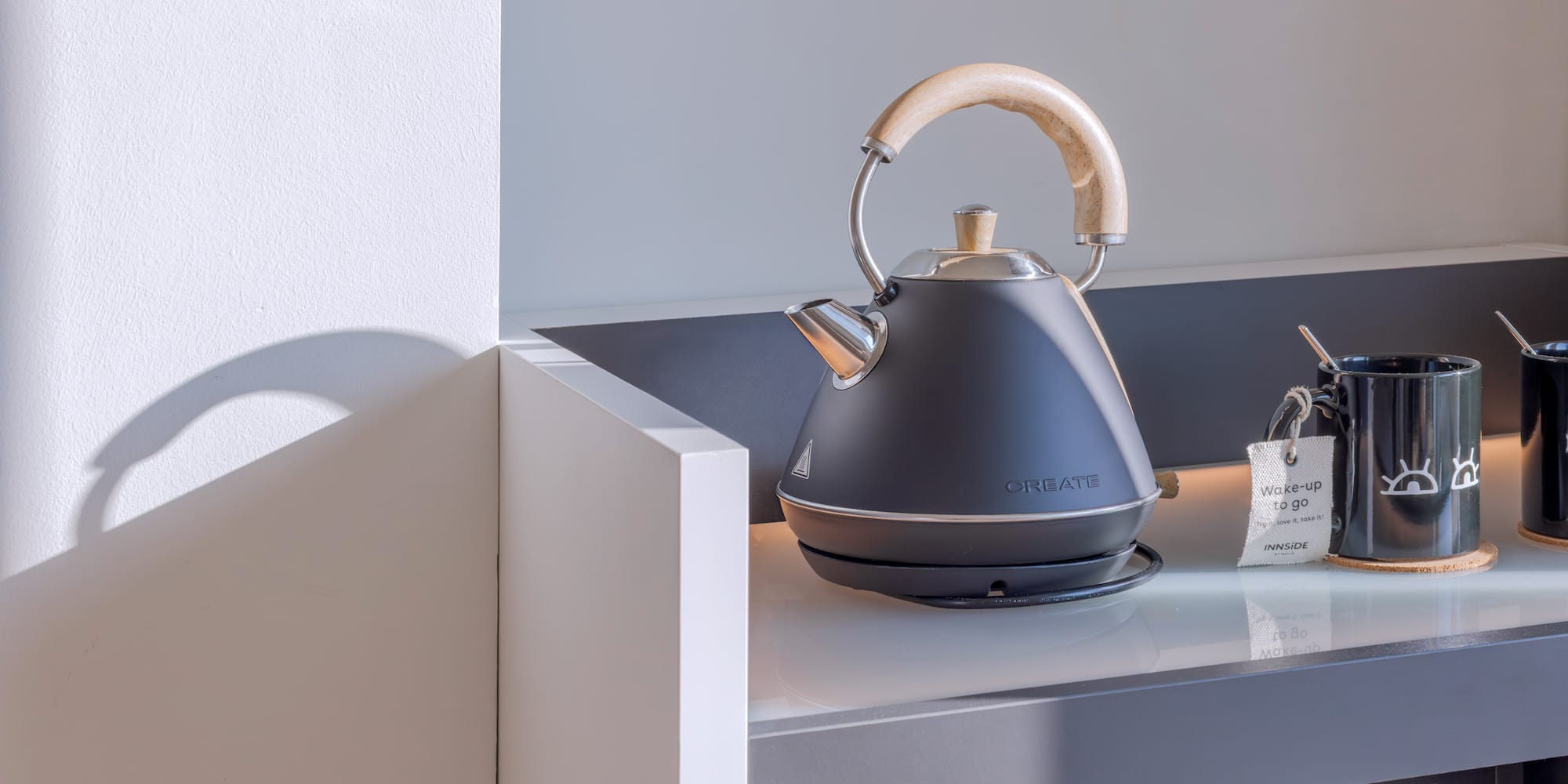 Tetera eléctrica negra, tazas de café/té en mostrador para desayuno.