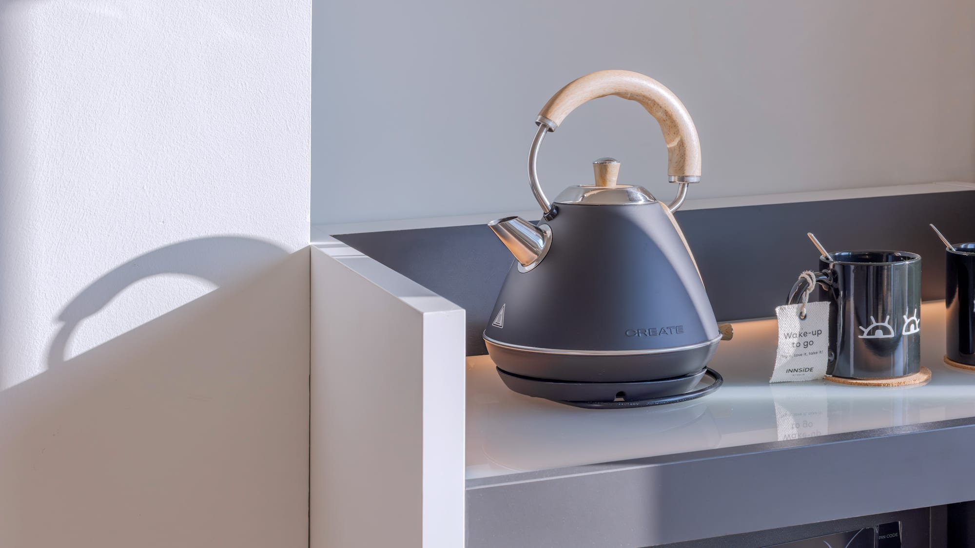 Tetera eléctrica negra, tazas de café/té en mostrador para desayuno.