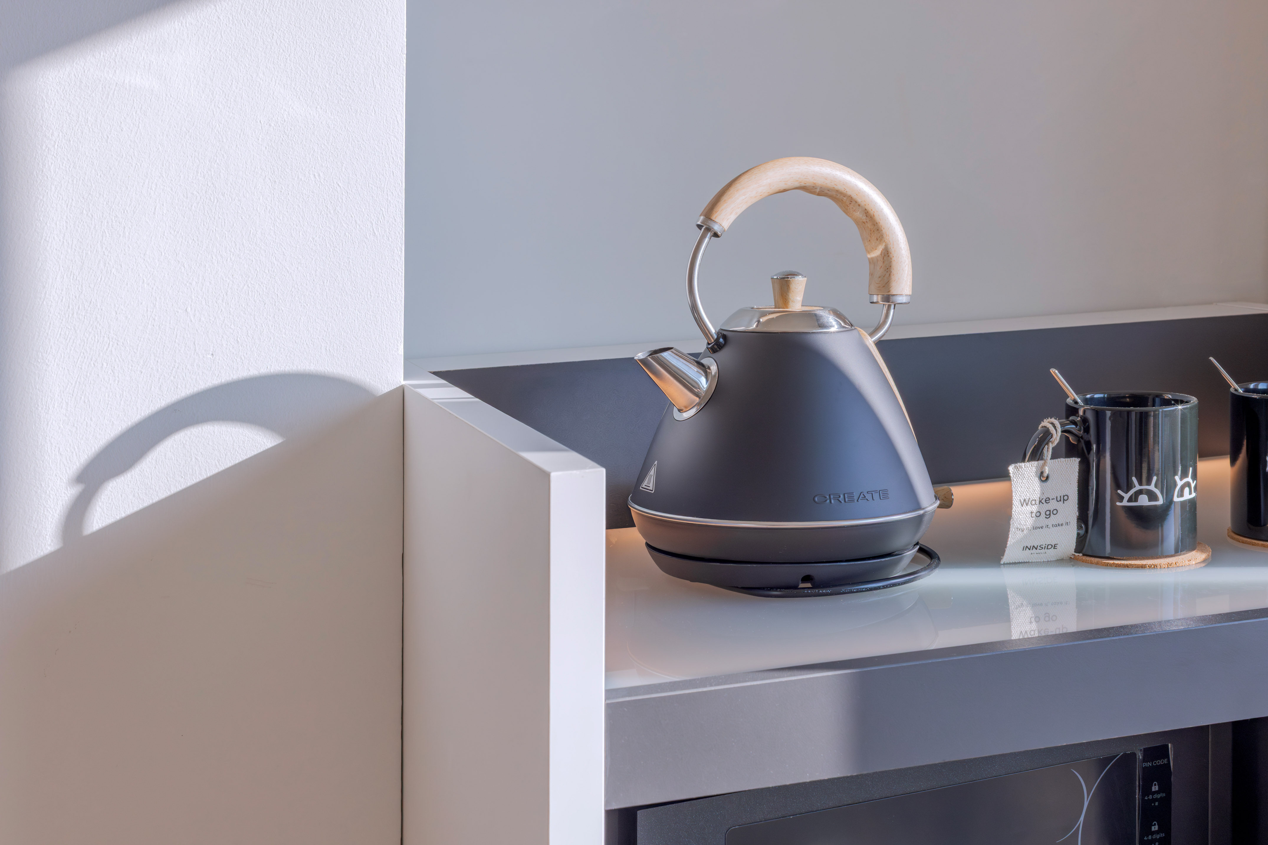 Tetera eléctrica negra, tazas de café/té en mostrador para desayuno.
