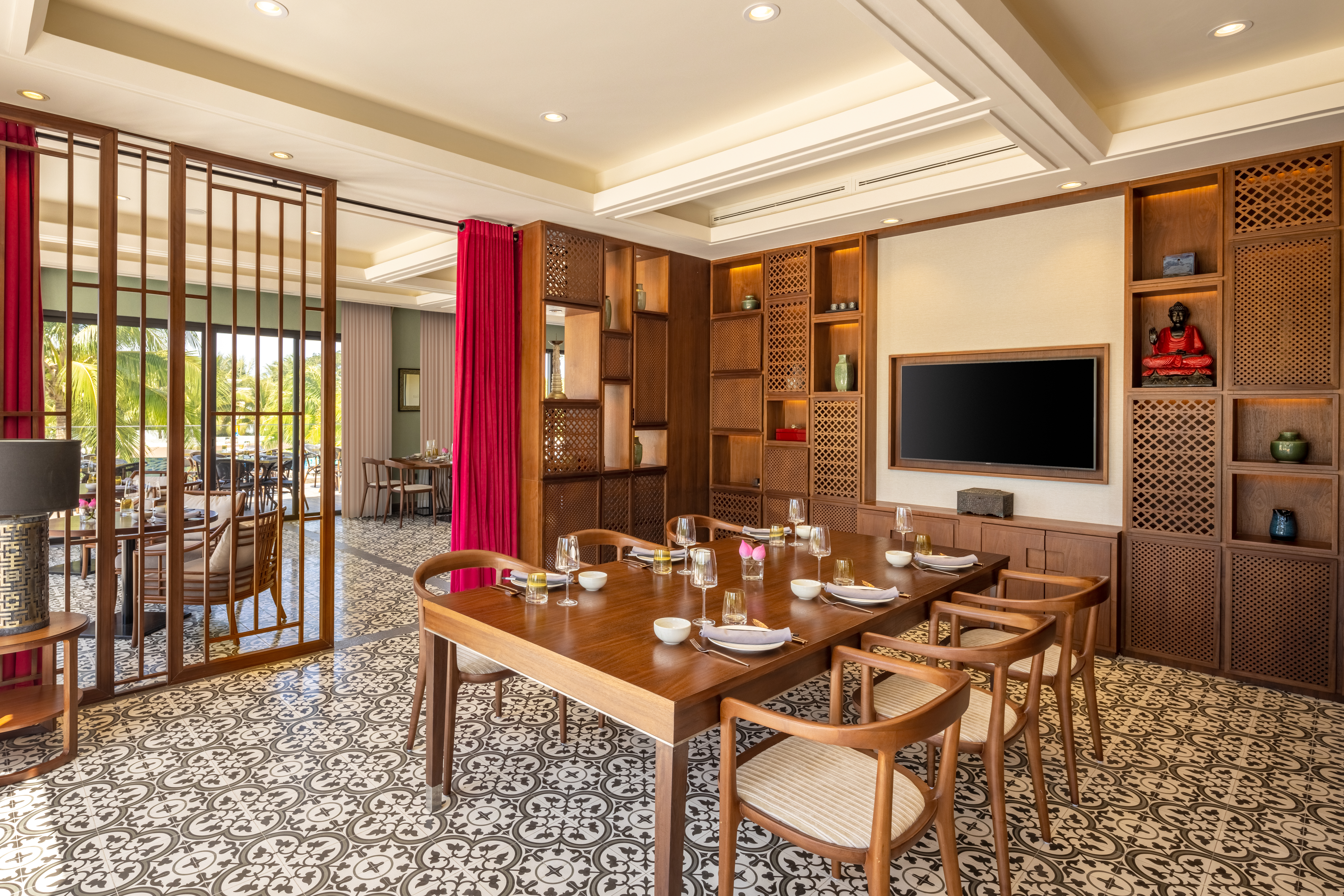 Asian dining room with wooden table, patterned floor, Buddha statue, and tropical view.