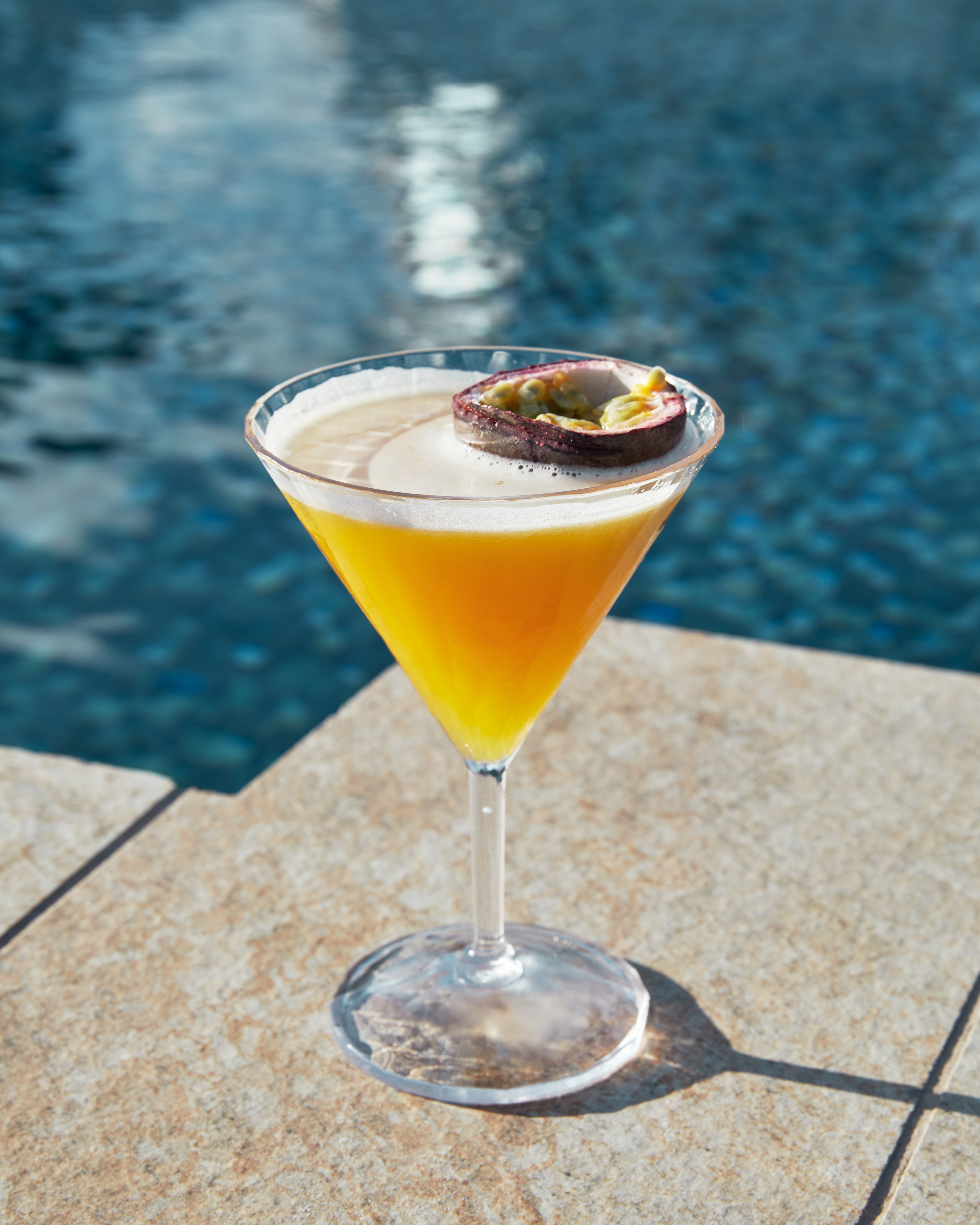 a glass of orange liquid with a slice of passion fruit on top of it