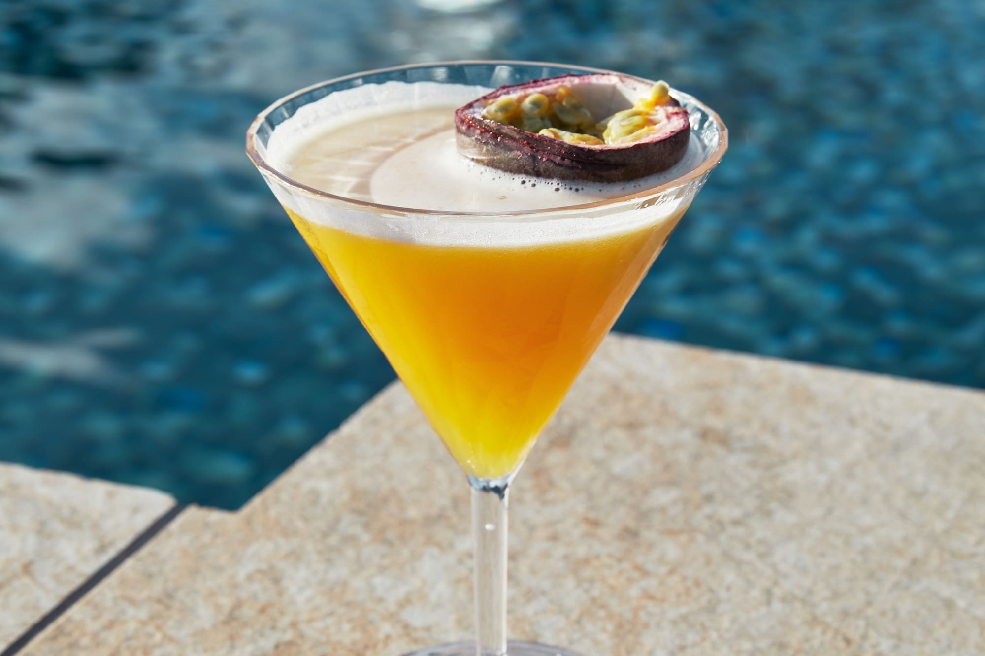 a glass of orange liquid with a slice of passion fruit on top of it