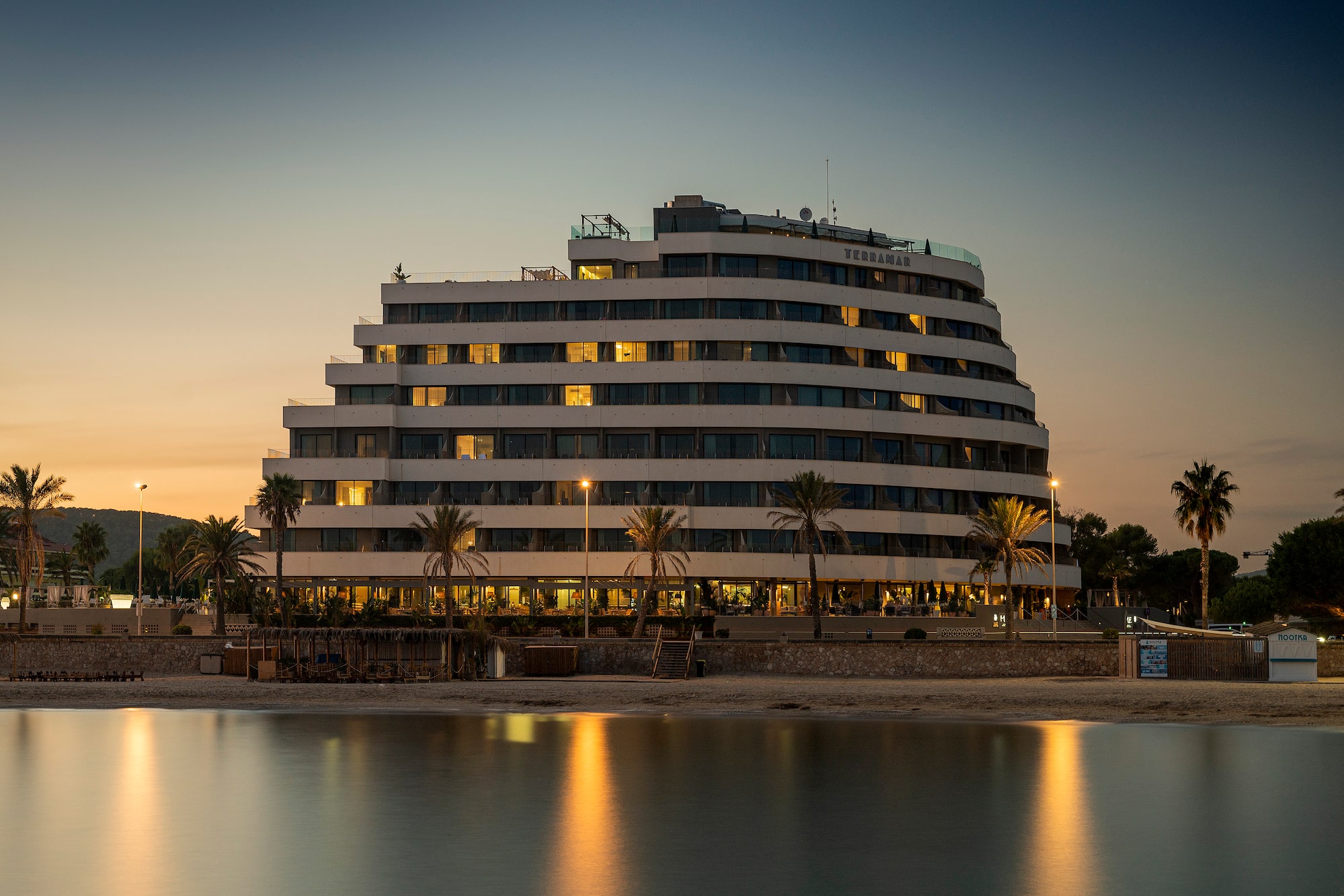 Beachfront Hotel Terramar glowing at dusk, lights reflecting in water.