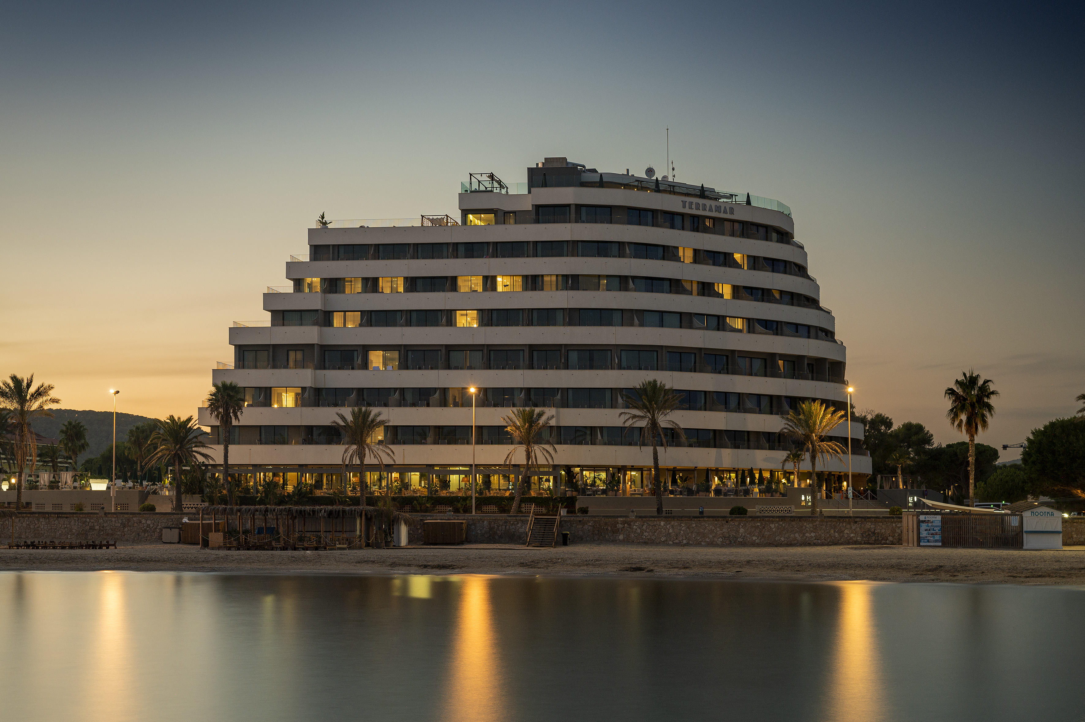 Beachfront Hotel Terramar glowing at dusk, lights reflecting in water.