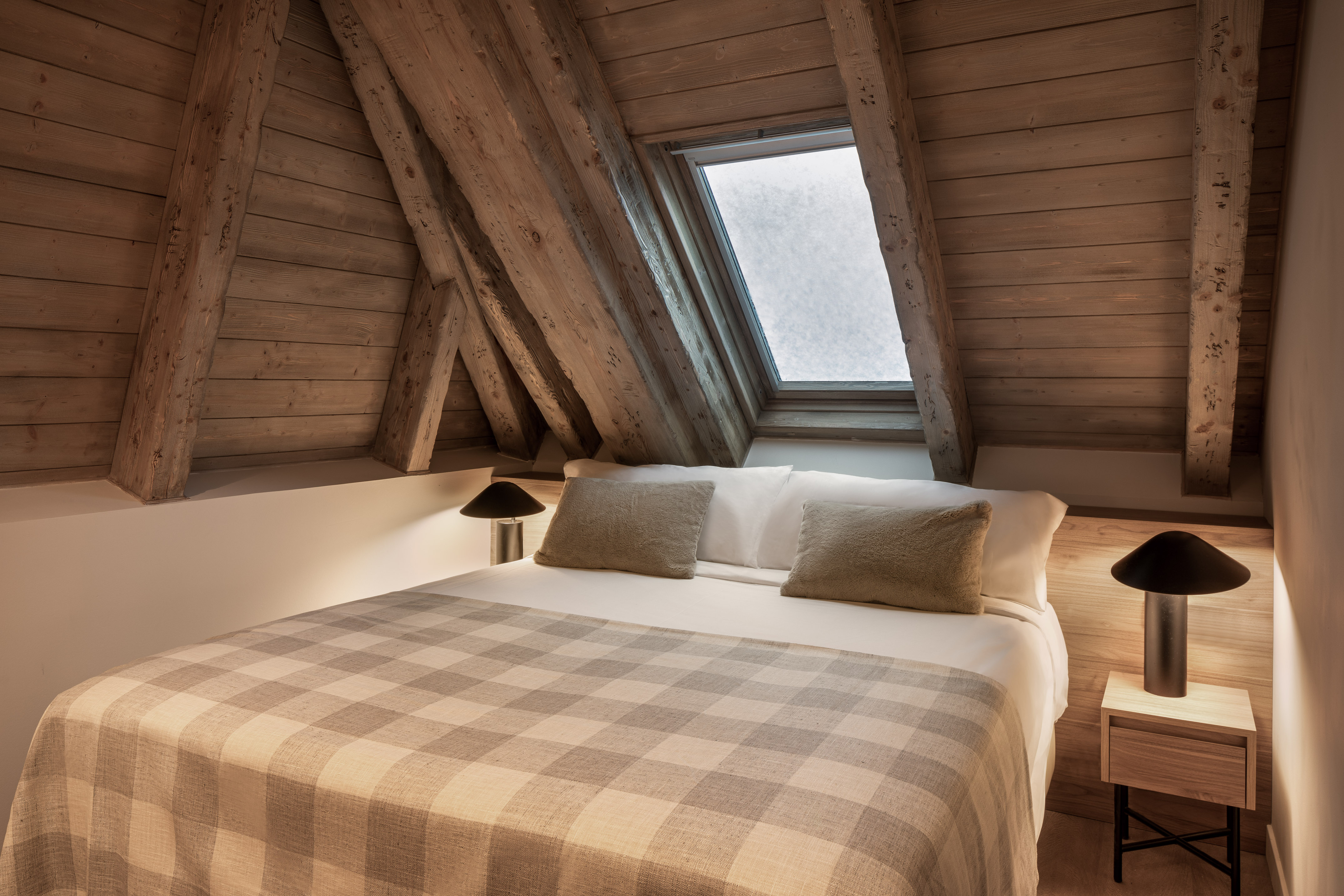 Cozy attic bedroom with wooden beams, skylight, and plaid blanket.