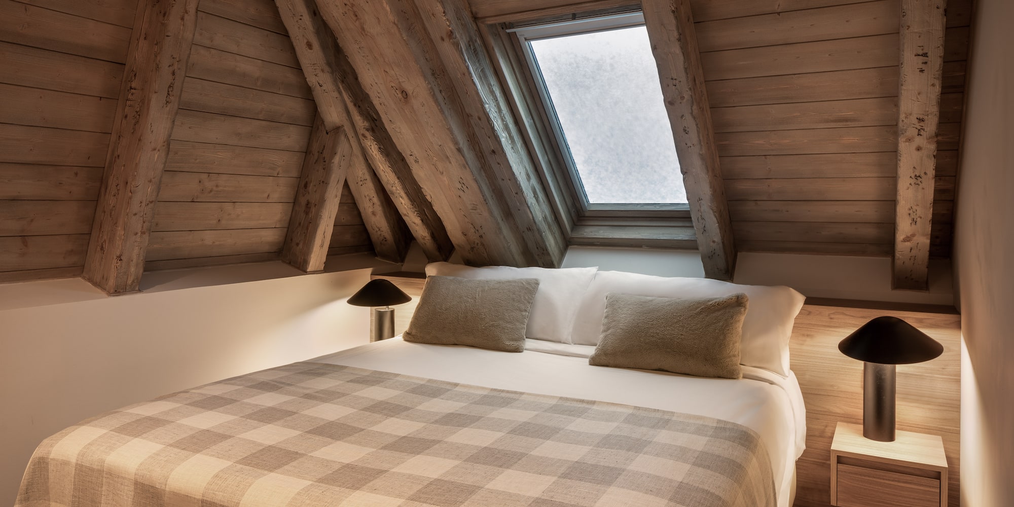Cozy attic bedroom with wooden beams, skylight, and plaid blanket.