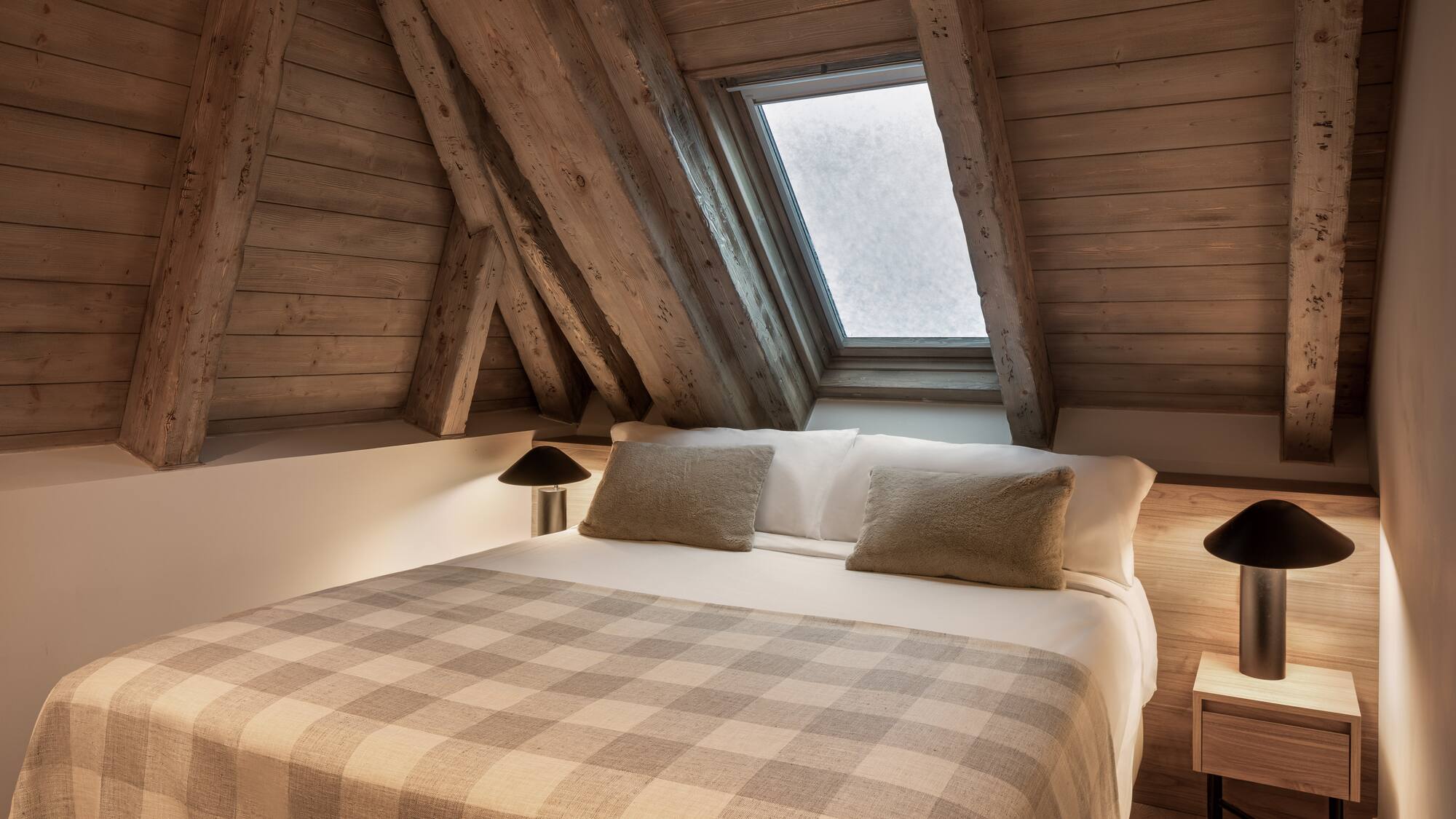 Cozy attic bedroom with wooden beams, skylight, and plaid blanket.