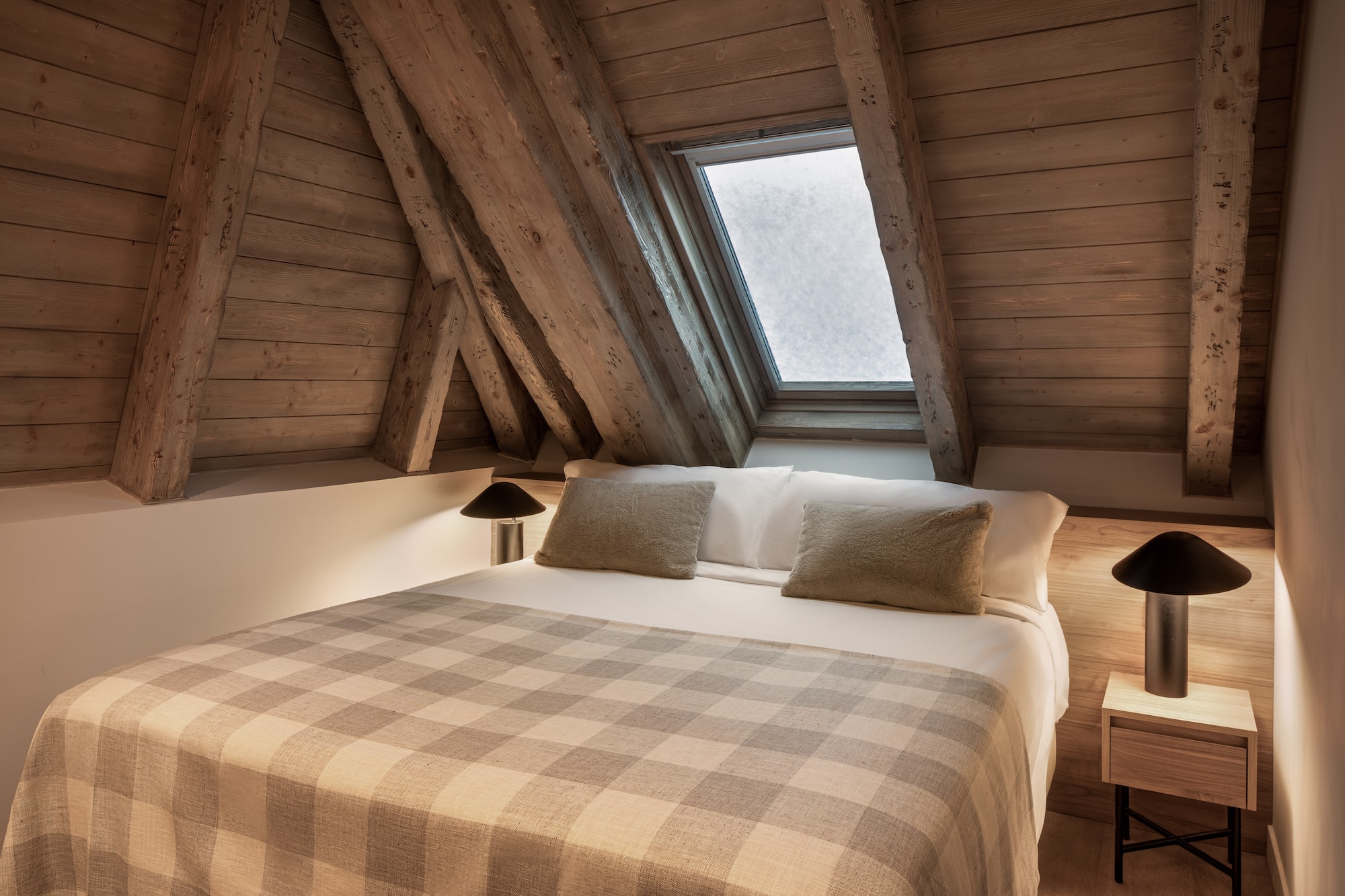 Cozy attic bedroom with wooden beams, skylight, and plaid blanket.