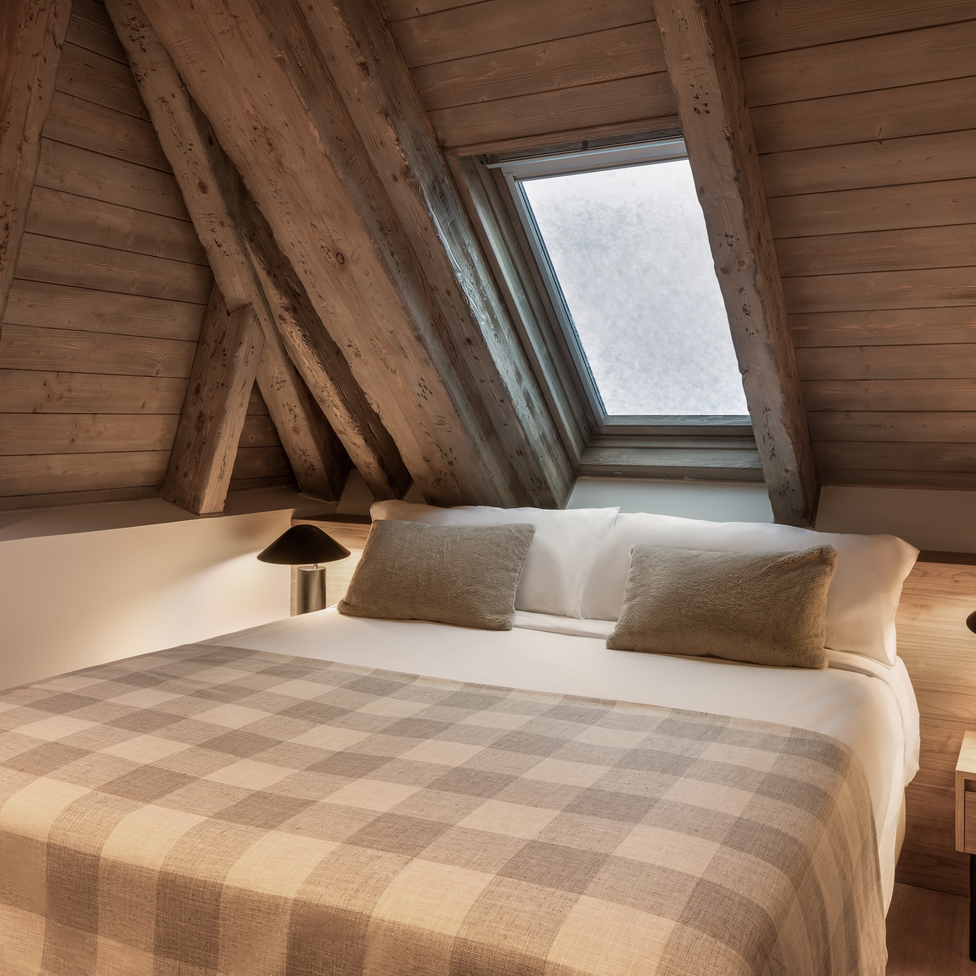 Cozy attic bedroom with wooden beams, skylight, and plaid blanket.