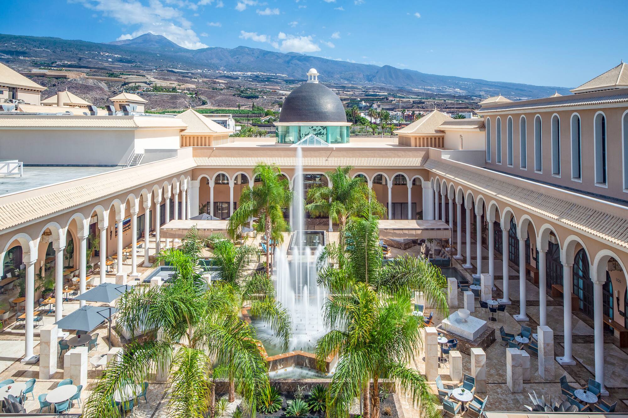 Luxury resort courtyard, fountain, palm trees, and Tenerife's Teide volcano.