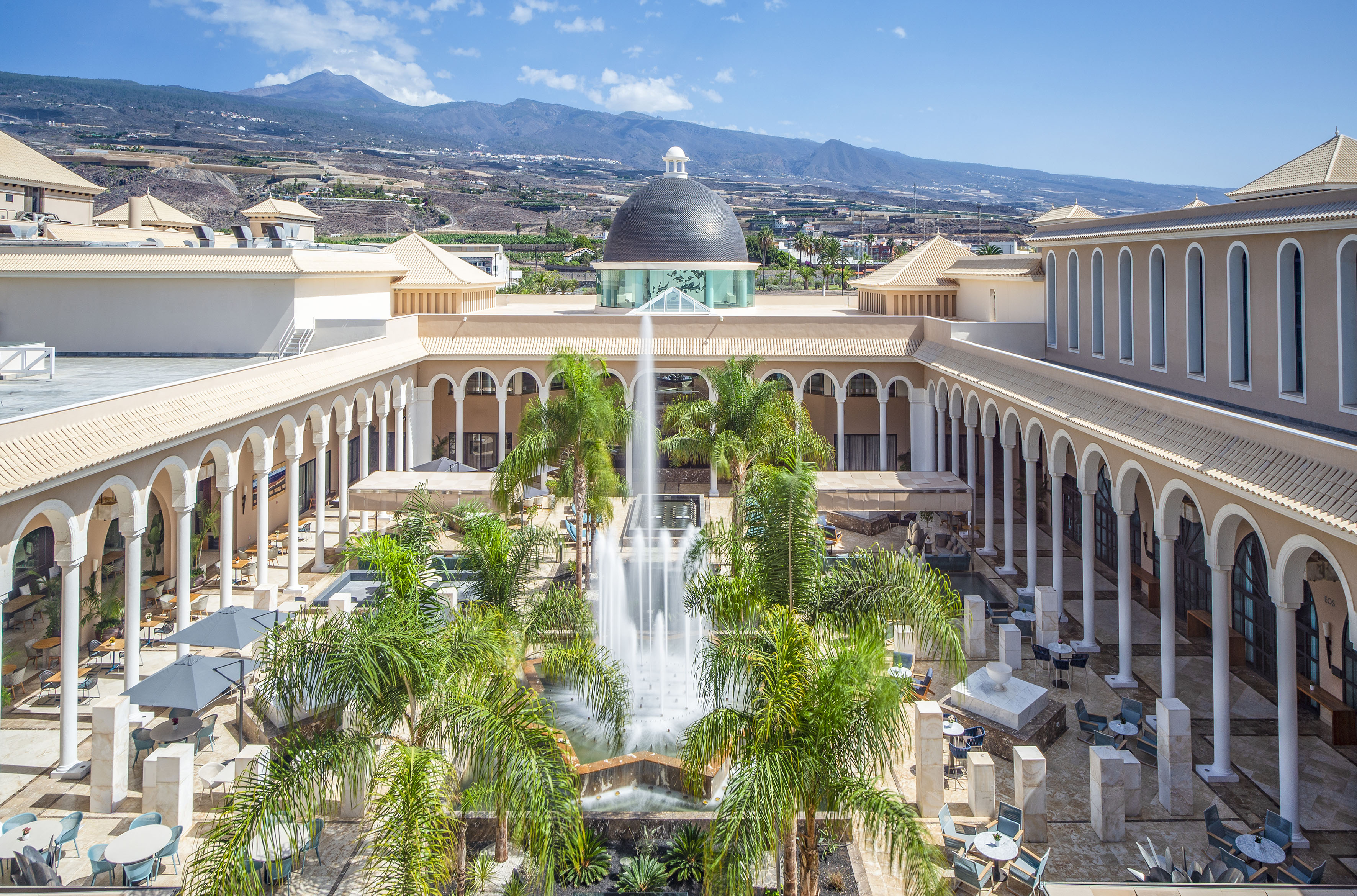 Luxury resort courtyard, fountain, palm trees, and Tenerife's Teide volcano.