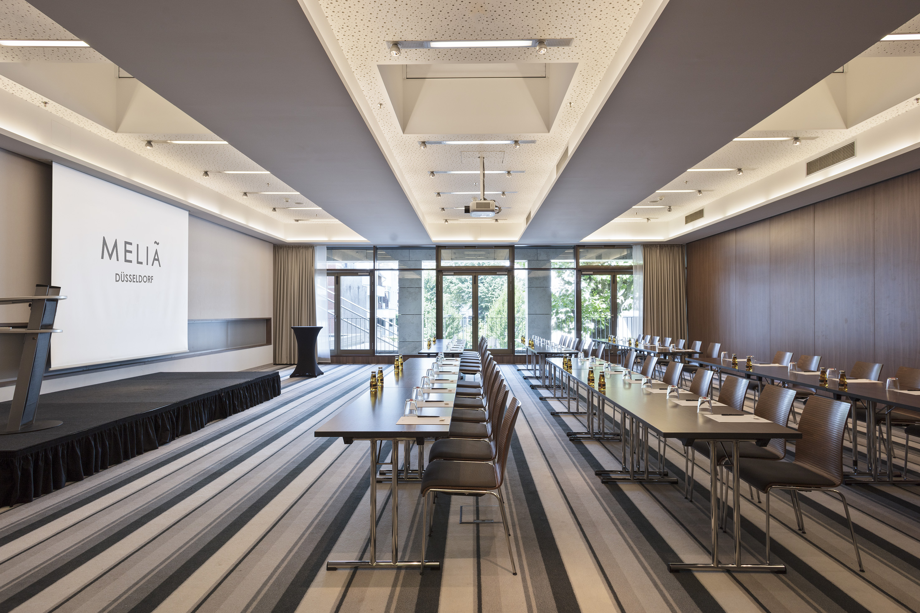 Modern Melia Düsseldorf meeting room with screen, projector, and tables set for events.
