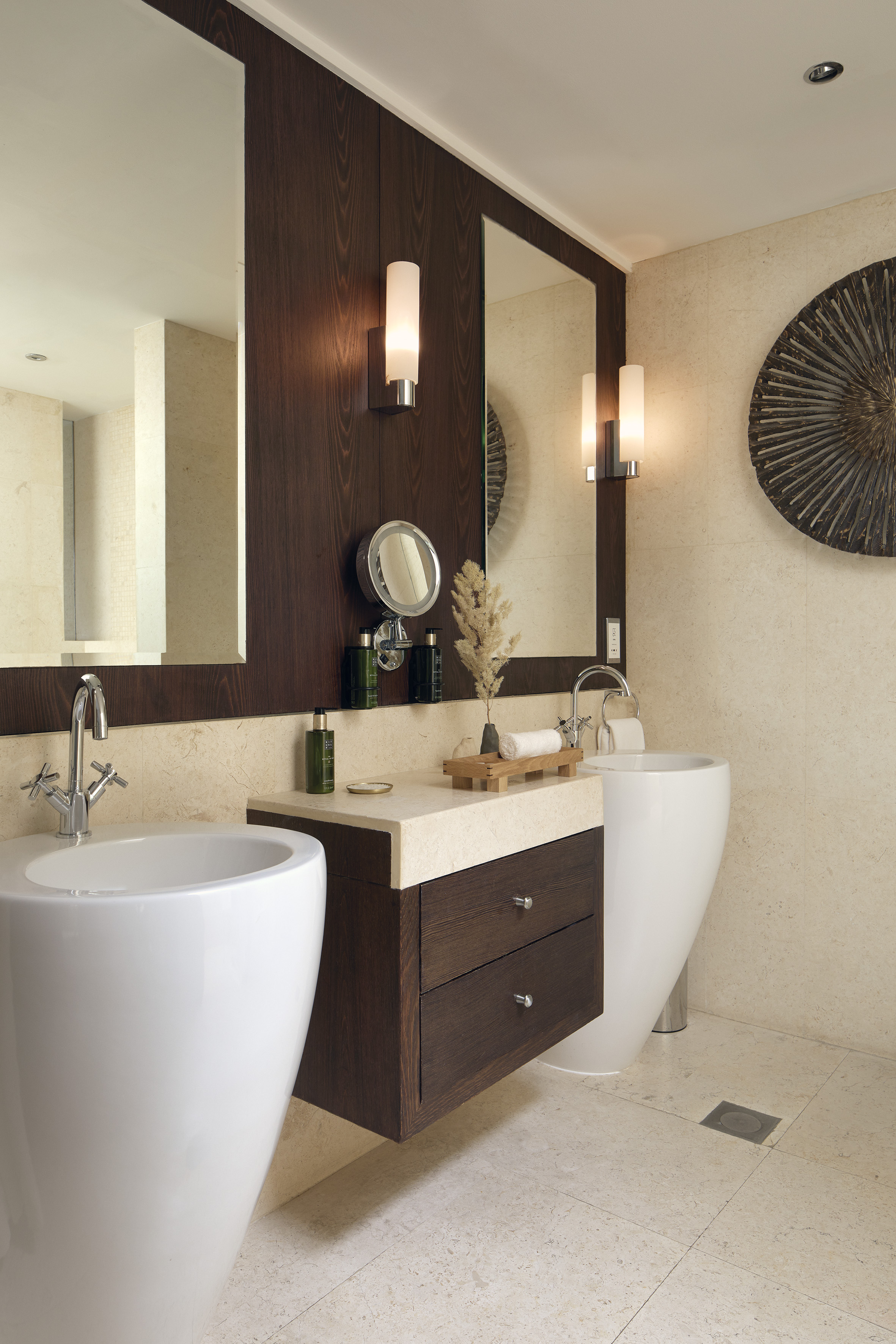 Modern luxury bathroom with dual sinks, dark wood vanity, large mirrors, marble walls.