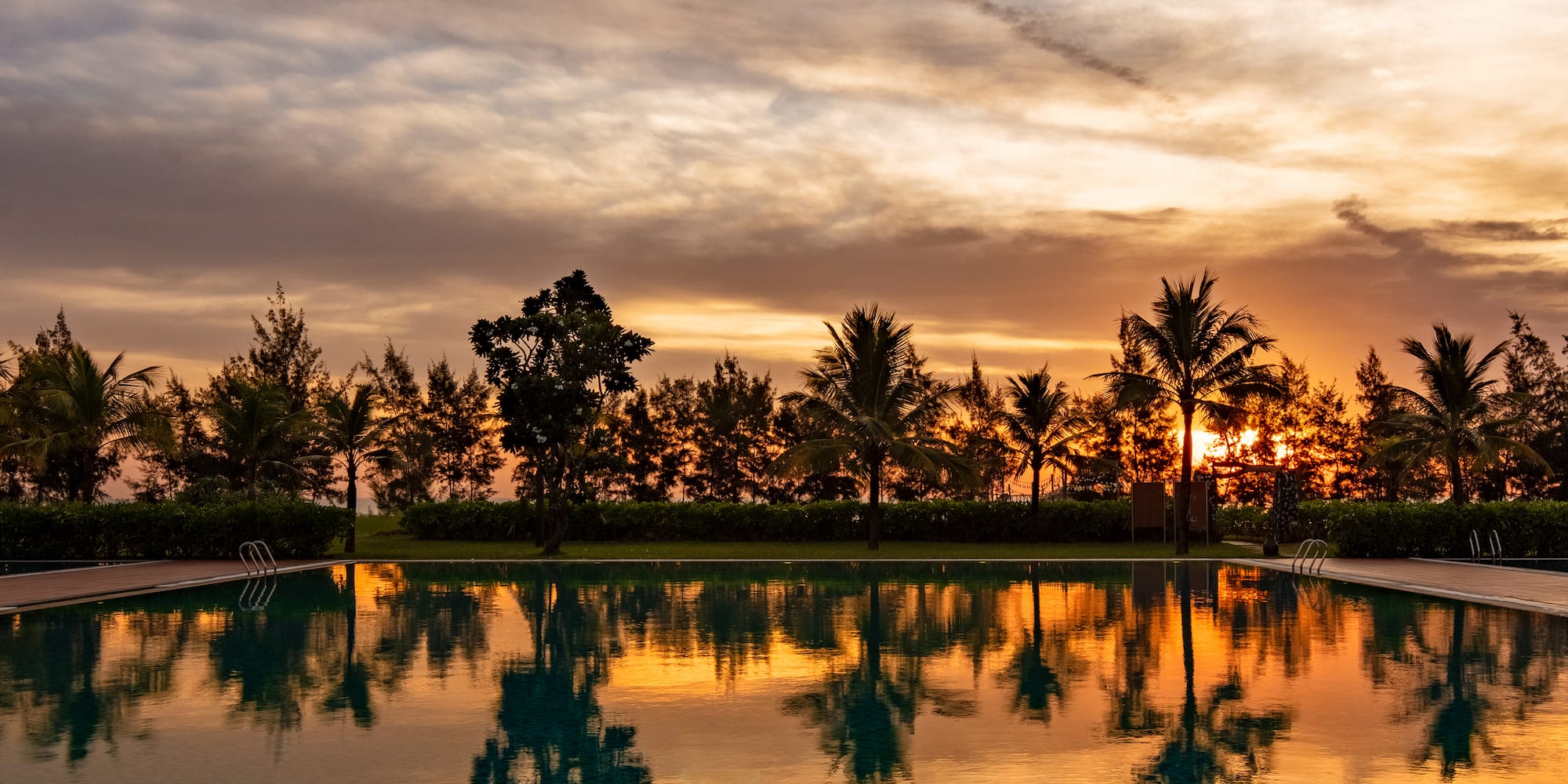 a pool with trees and a sunset